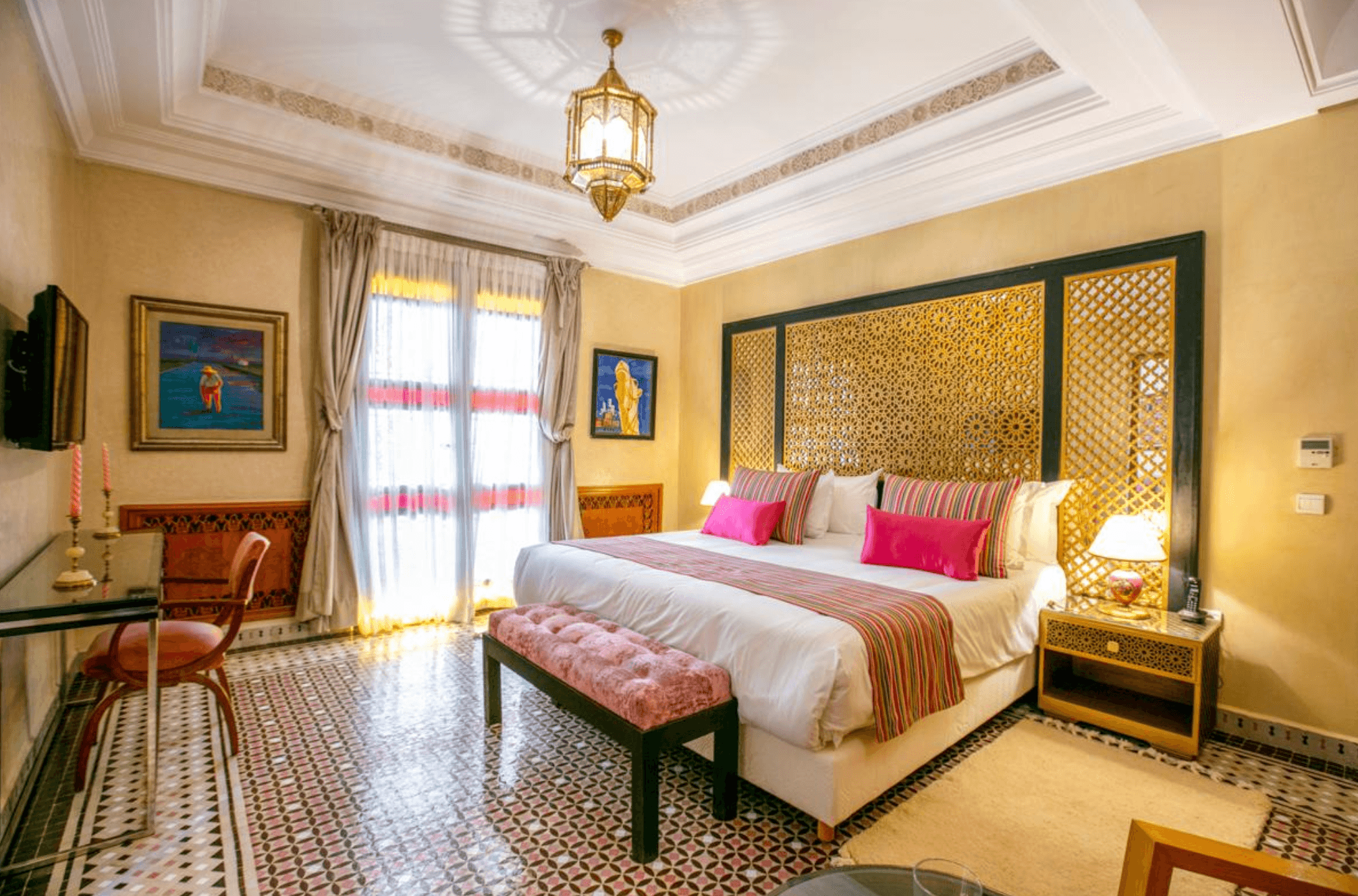 View of a pretty yellow and pink hued room in a villa with a large bed and small desk area
