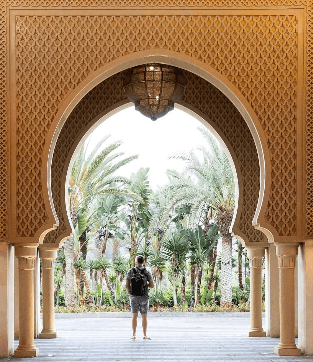Beautiful view of a person standing under a Moroccan-style archway and palm trees in the background