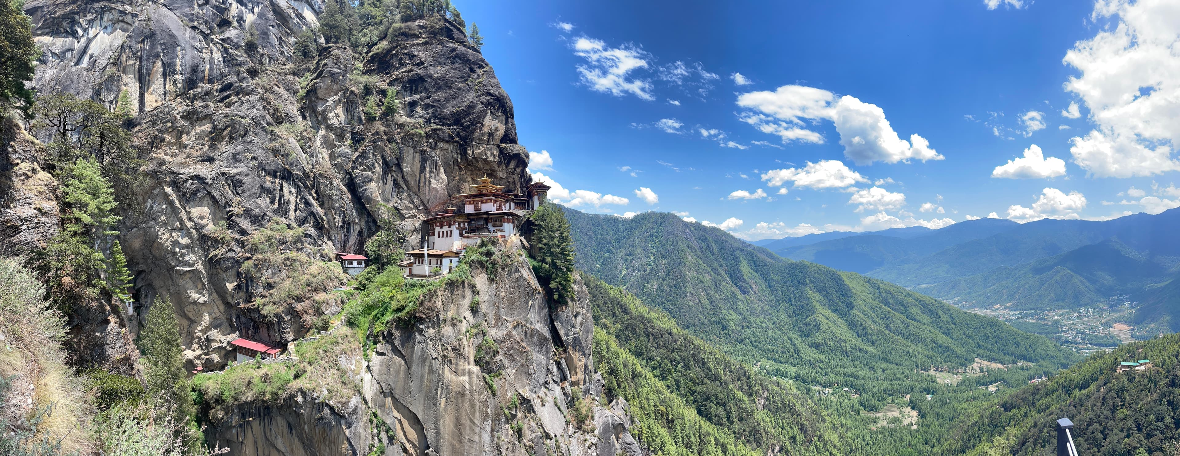 A view of a temple nestled into a mountain with stunning views and blue skies surrounding the mountainous terrain.