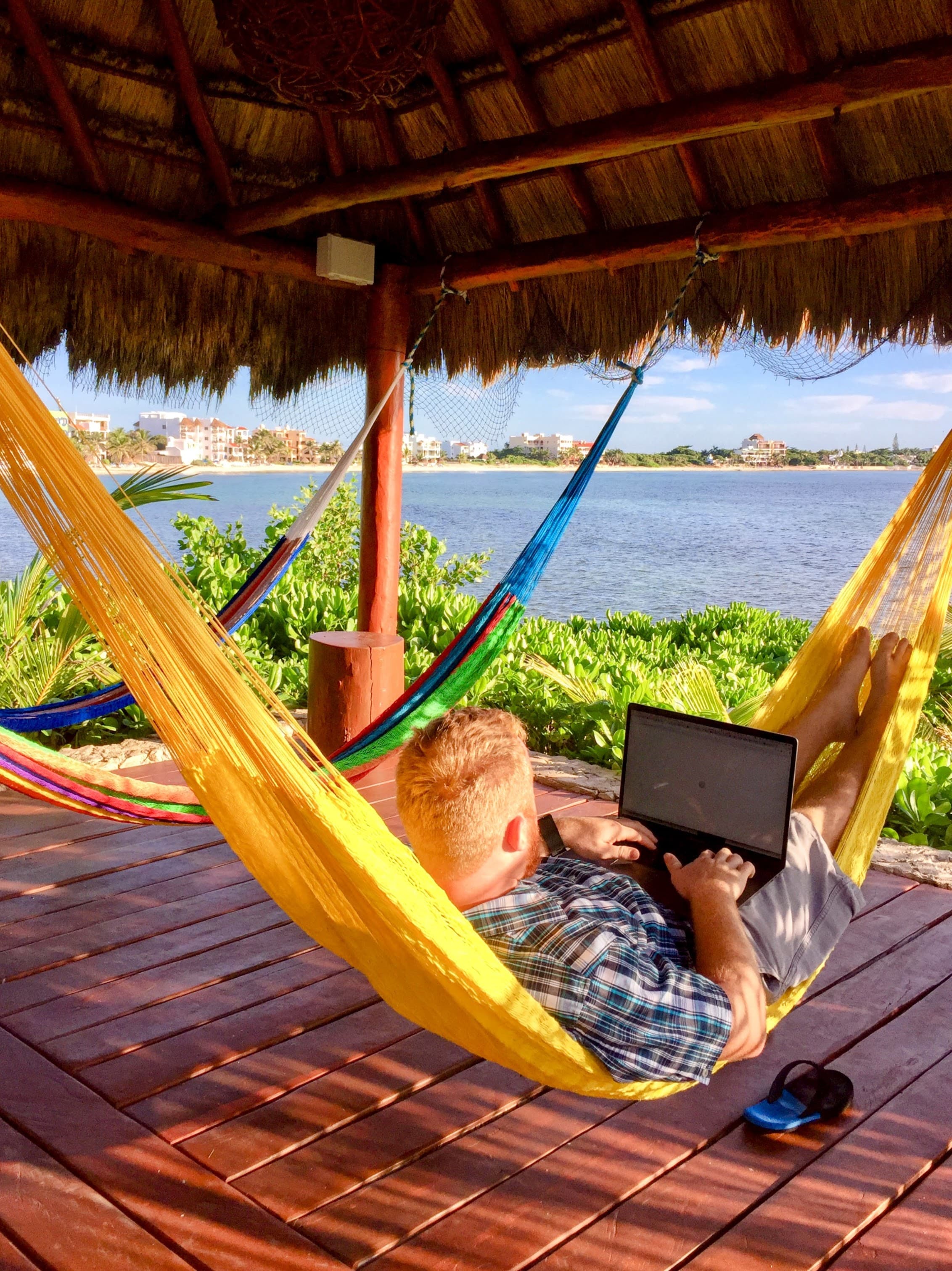 View of Mike laying in a yellow hammock overlooking the ocean while on his laptop