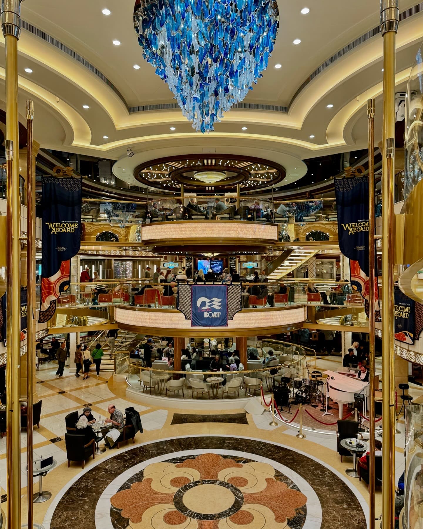 View of a two-story cruise ship lobby as passengers mill the lounge.