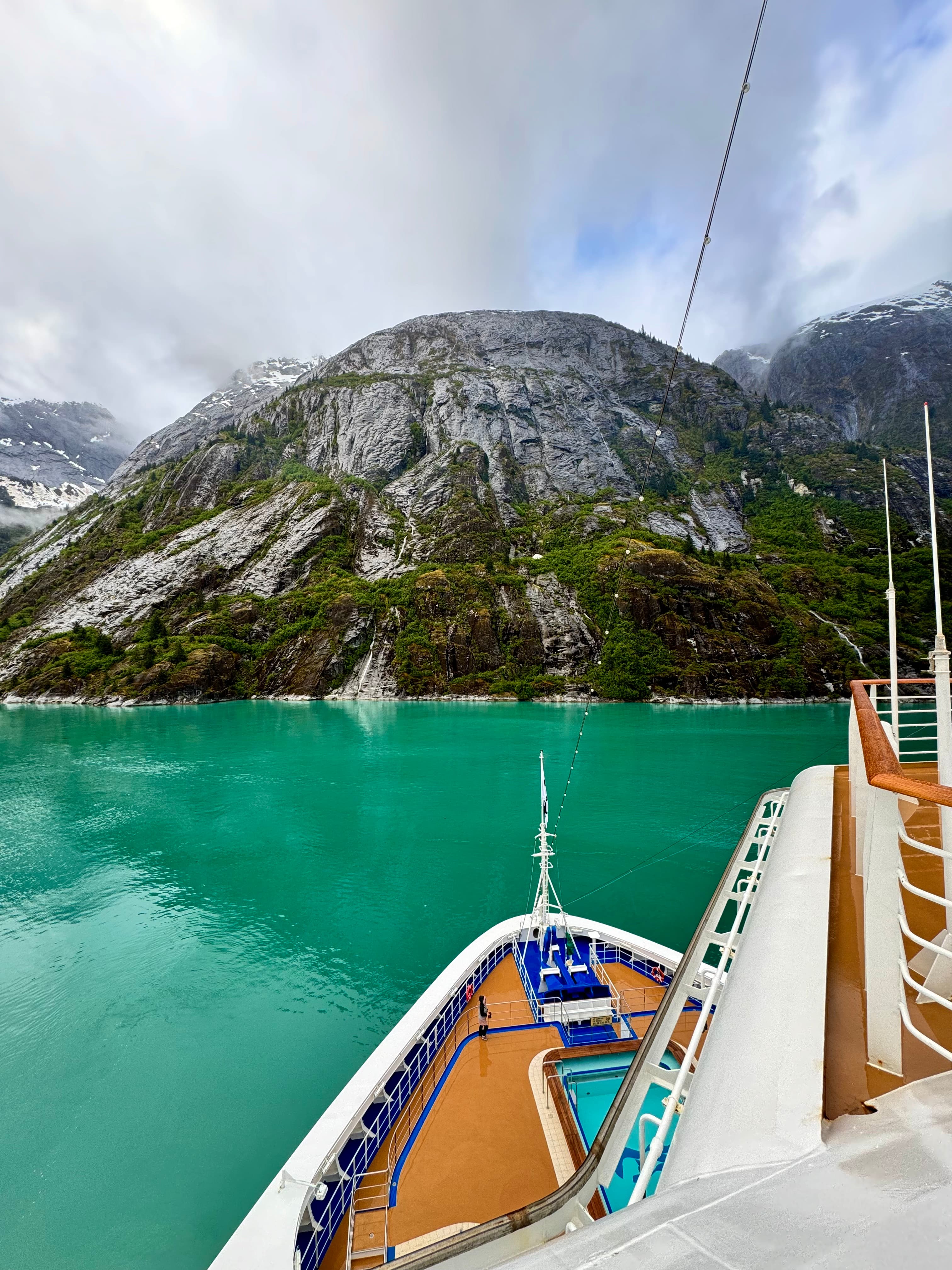 Crystal clear waters gently lap near the prow of a boat near the shore of a rocky crag covered in moss on a sunny day.