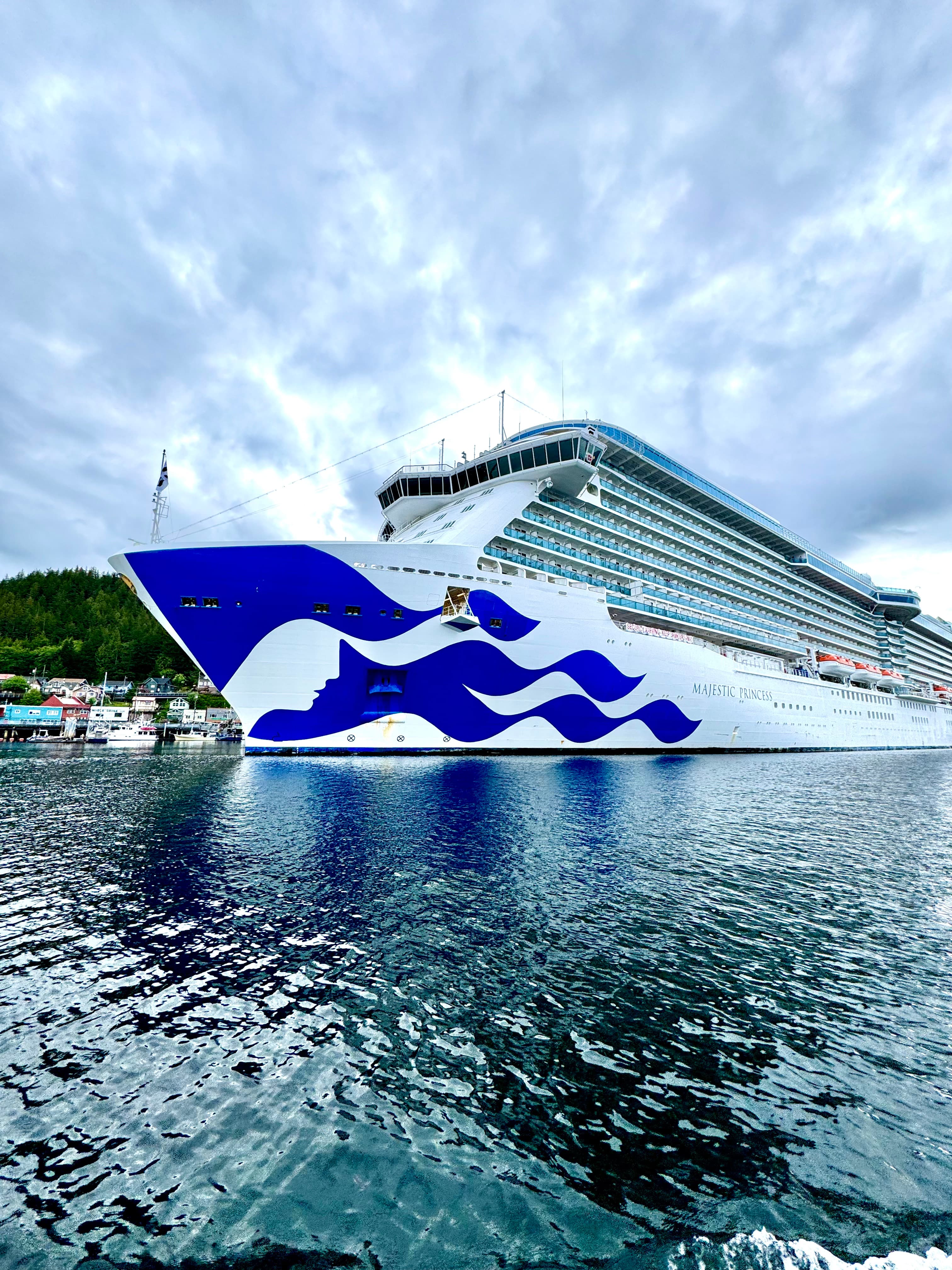 A cruise ship leaving dock as the waves gently lap the shore on a cloudy day.