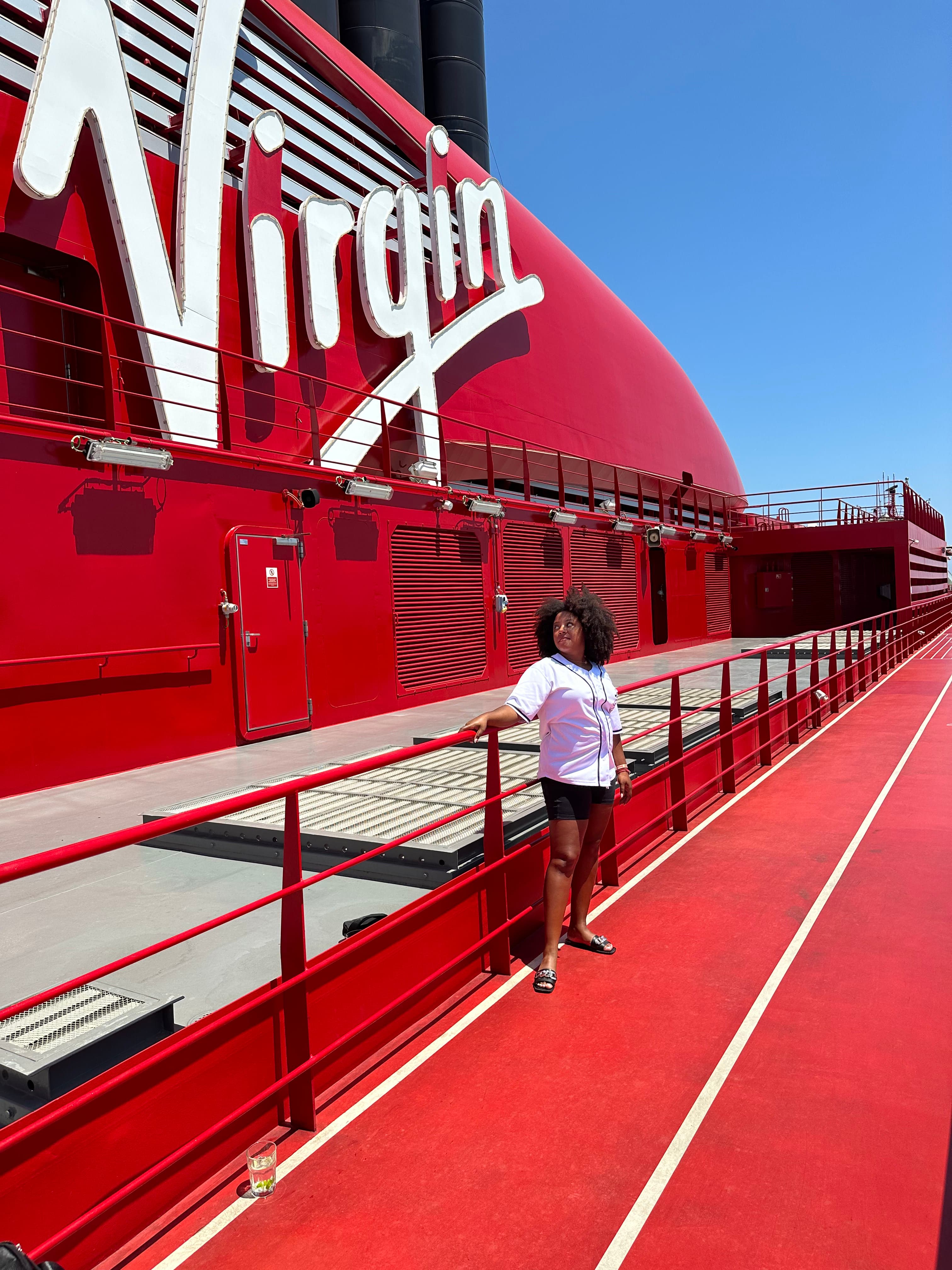Woman in a white shirt posing against a railing in front of a red Virgin sign.