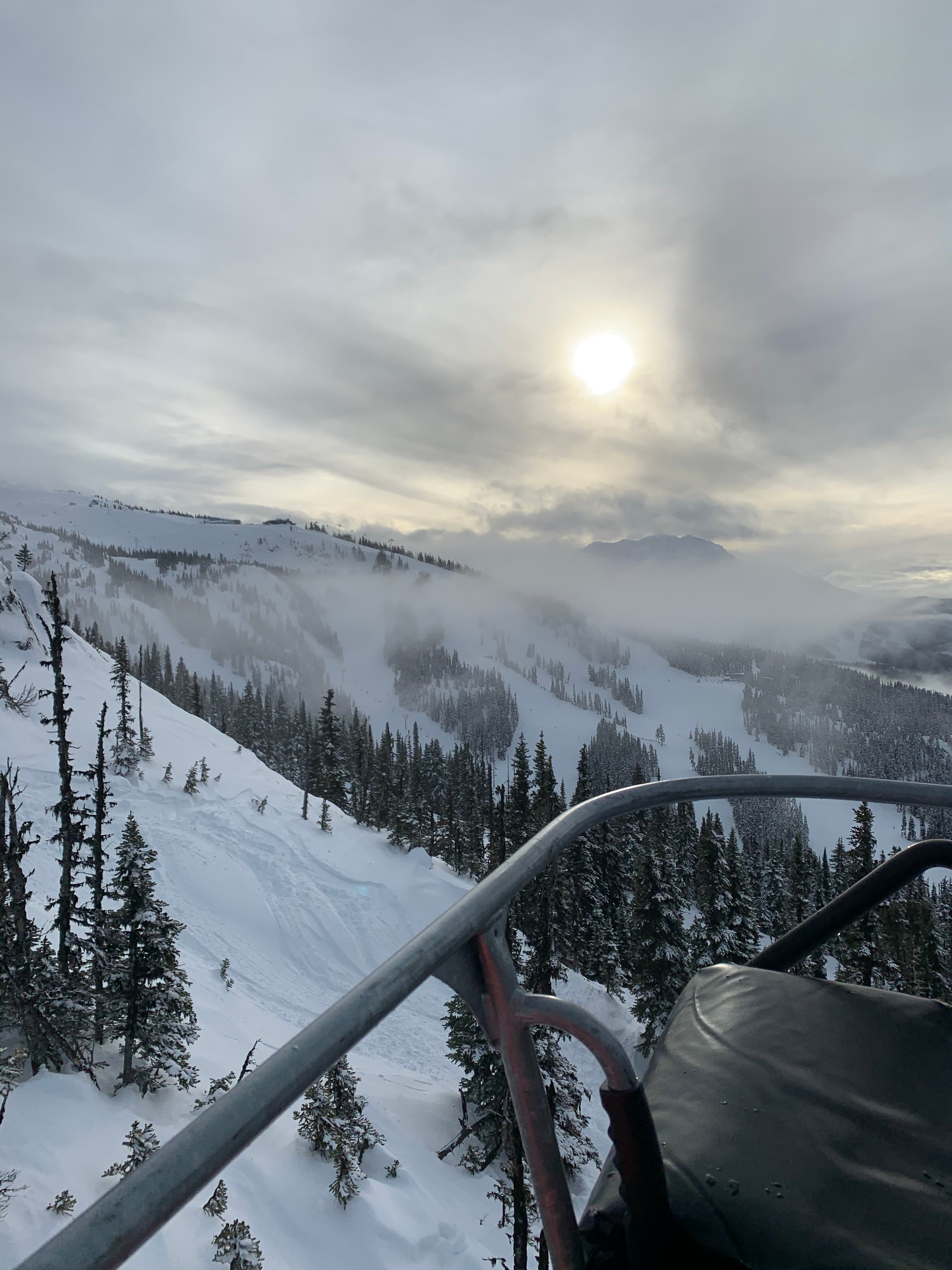 Snowy mountain landscape with a ski lift, trees and distant mountains.