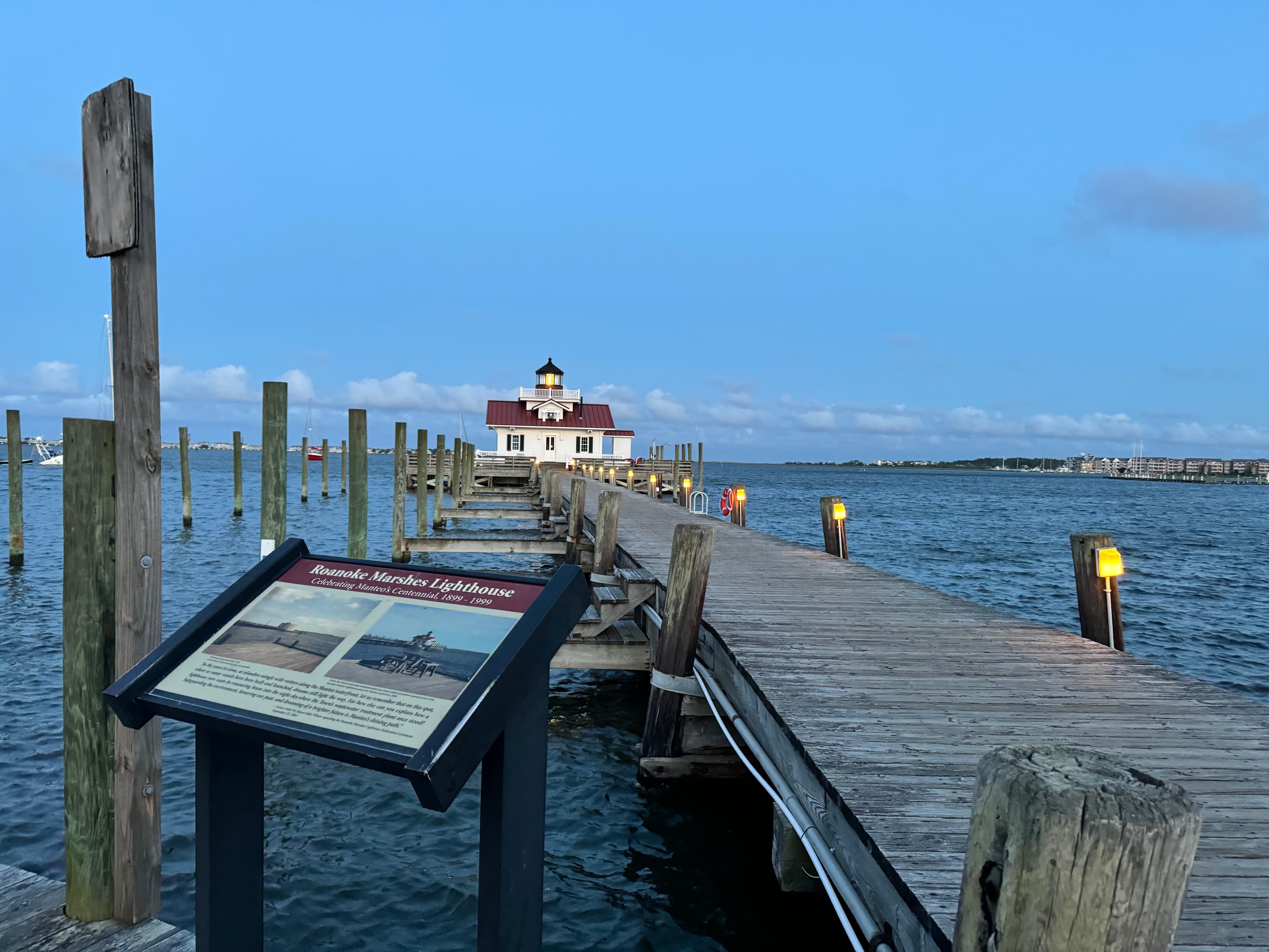 A dock lined with lights that goes out to the ocean with a house at the end of the dock.