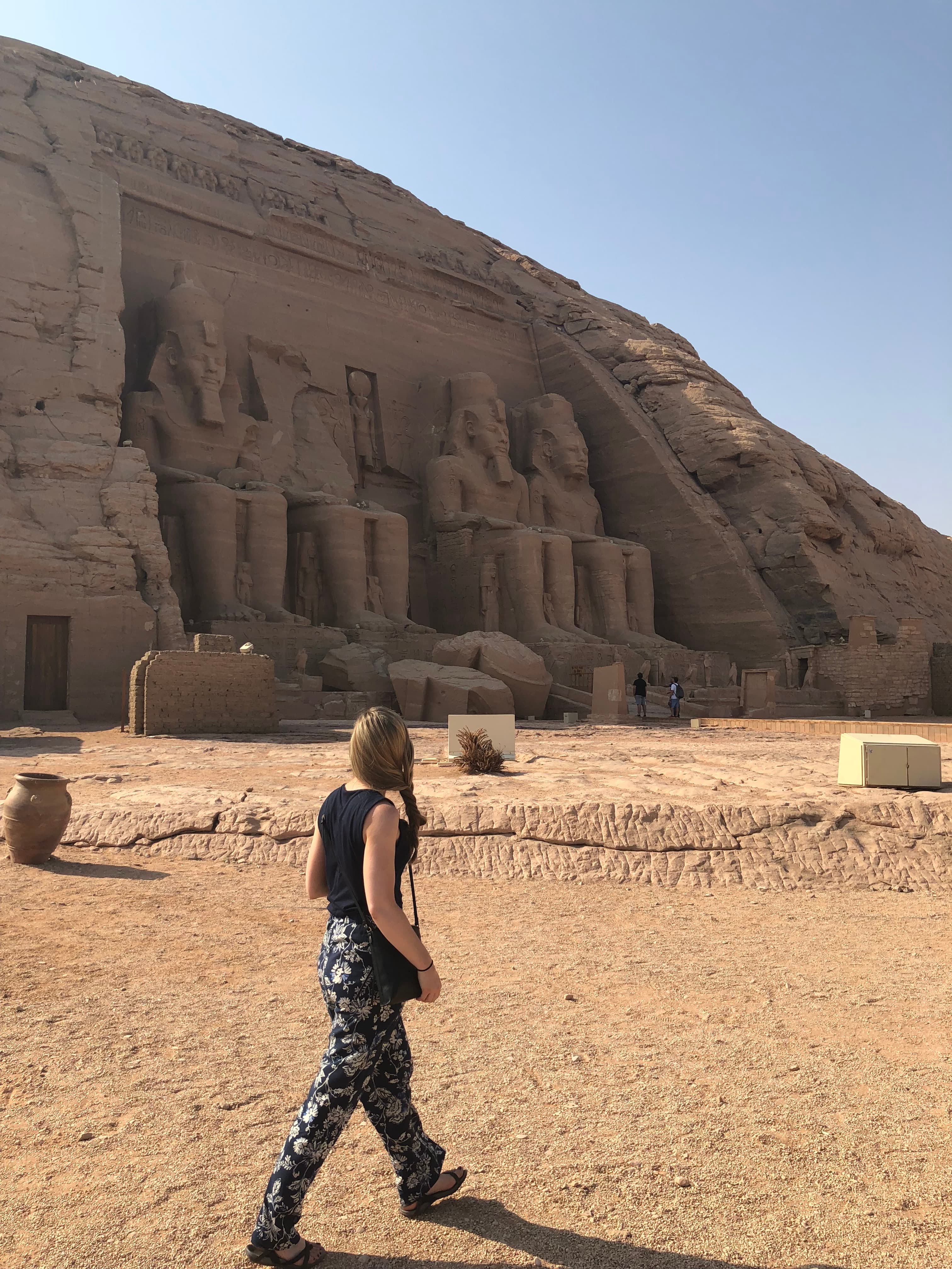 Woman walking towards large ancient rock carvings in the desert during the daytime.