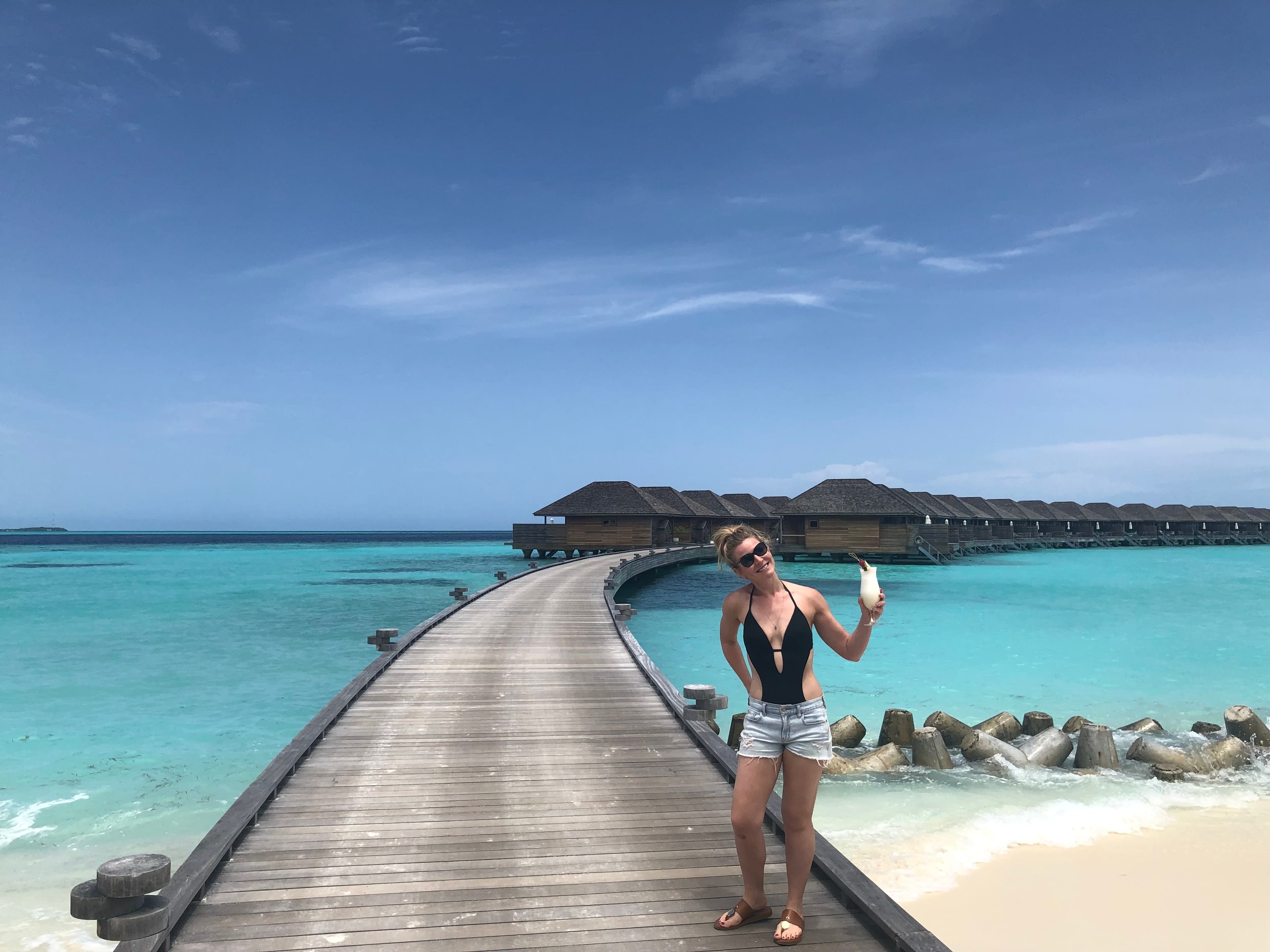 Advisor standing on wooden pier, looking out at sea with sandy beach in view.