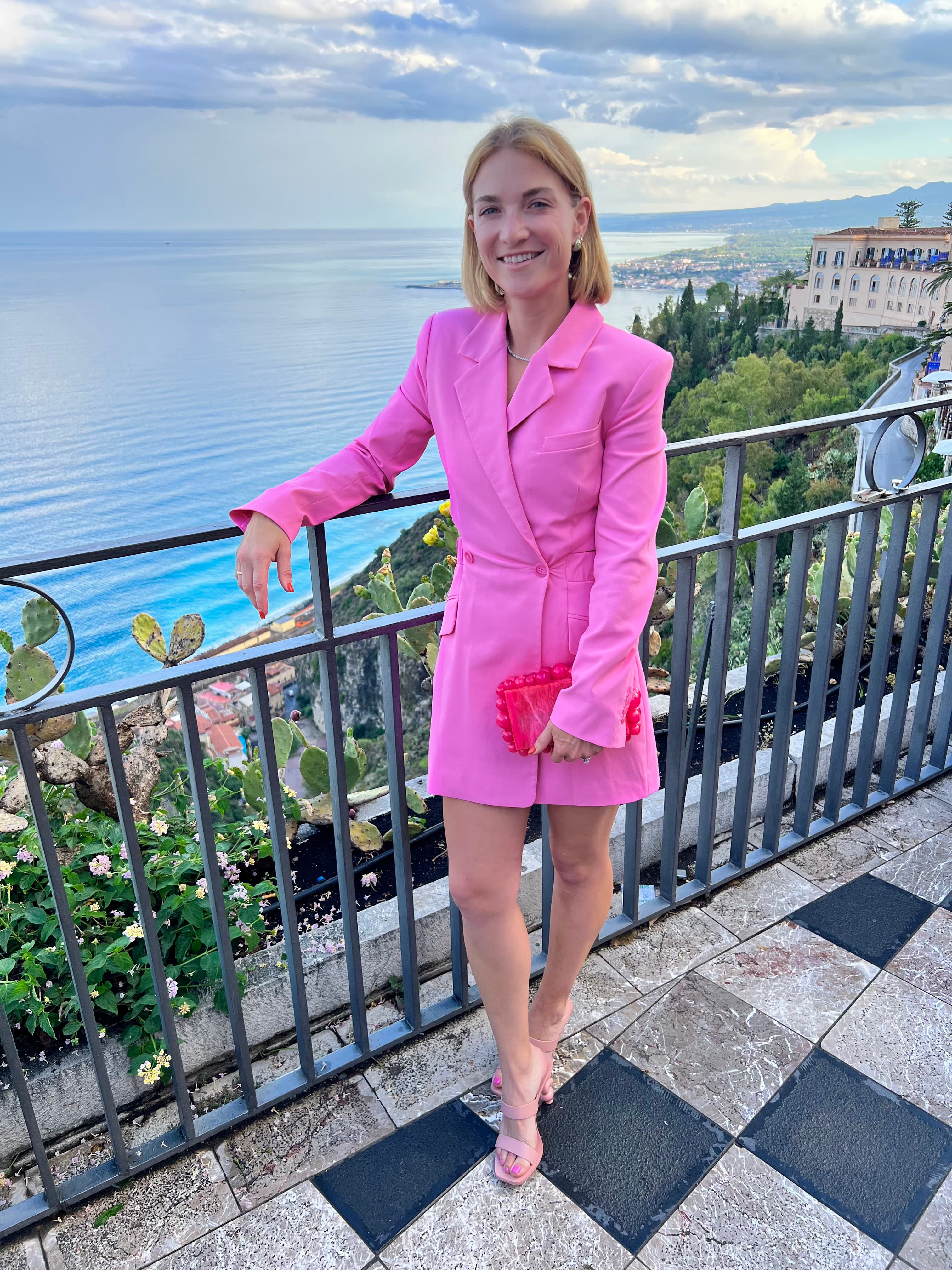 Advisor posing on a balcony with the ocean in the distance on a sunny day.