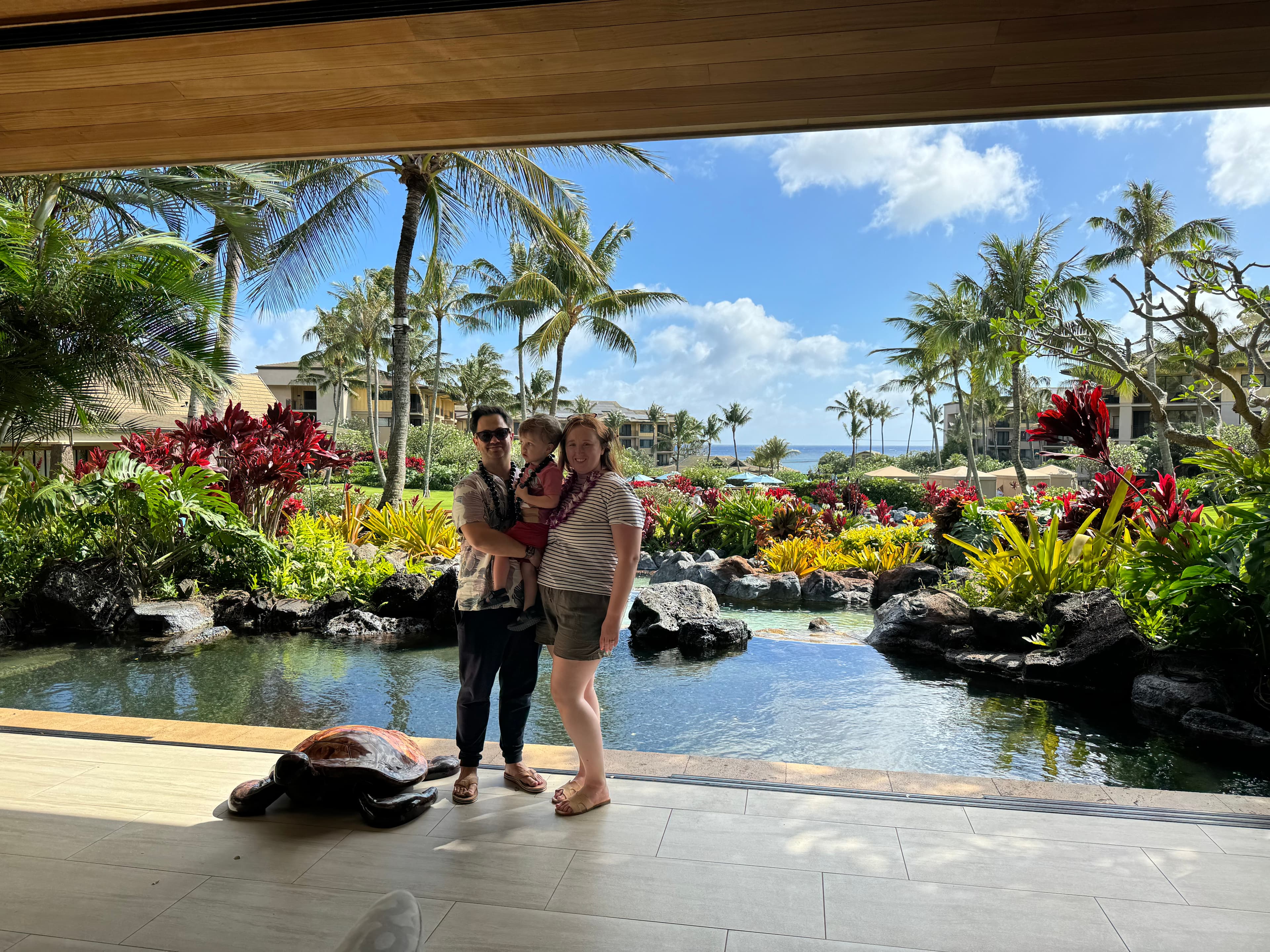 Briana and her family posing by a pond at a hotel resort surrounded by tropical plants on a sunny day