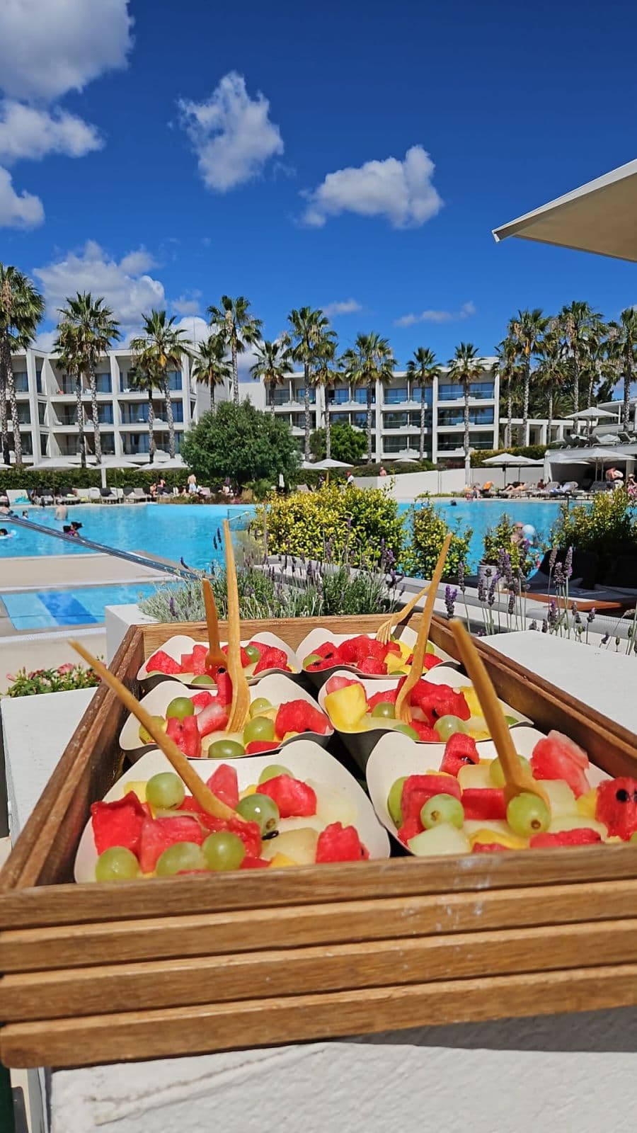 Poolside table set with a fruit tray and chairs in front of a resort.