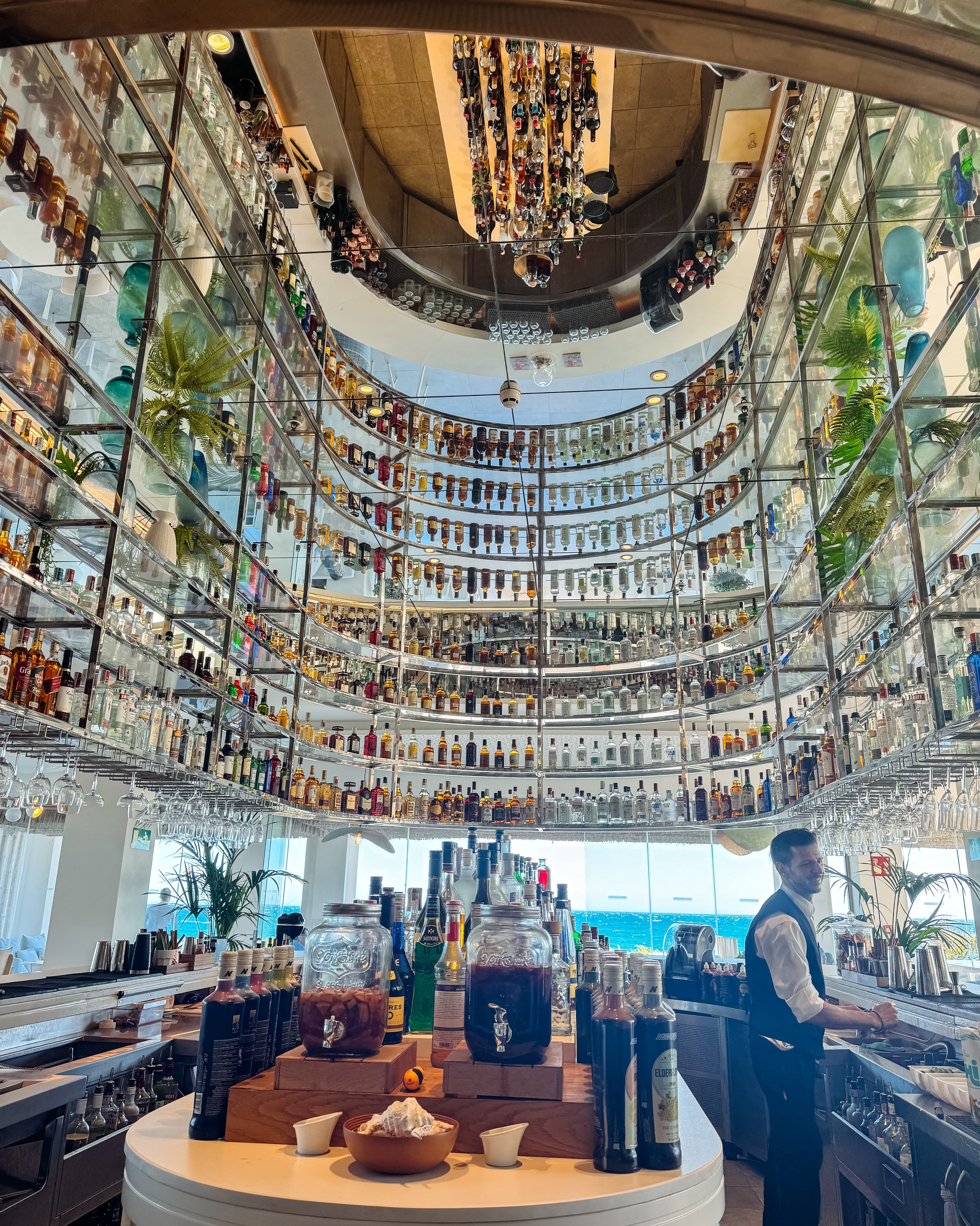 A luxurious bar with shelves full of bottles of alcohol, with the bartender making a drink.