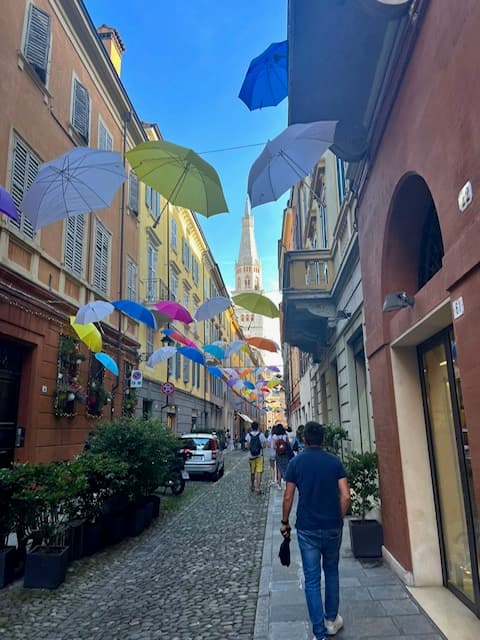 A person walking down a narrow street in between buildings, decorated with vibrant umbrellas.
