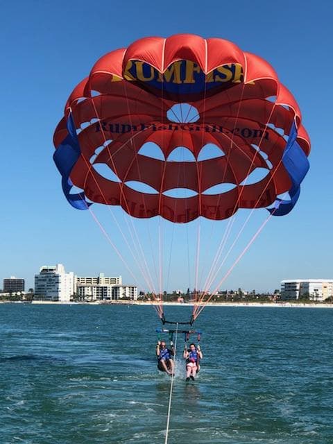 View of two people parasailing on a sunny day with a beach and buildings visible on the horizon