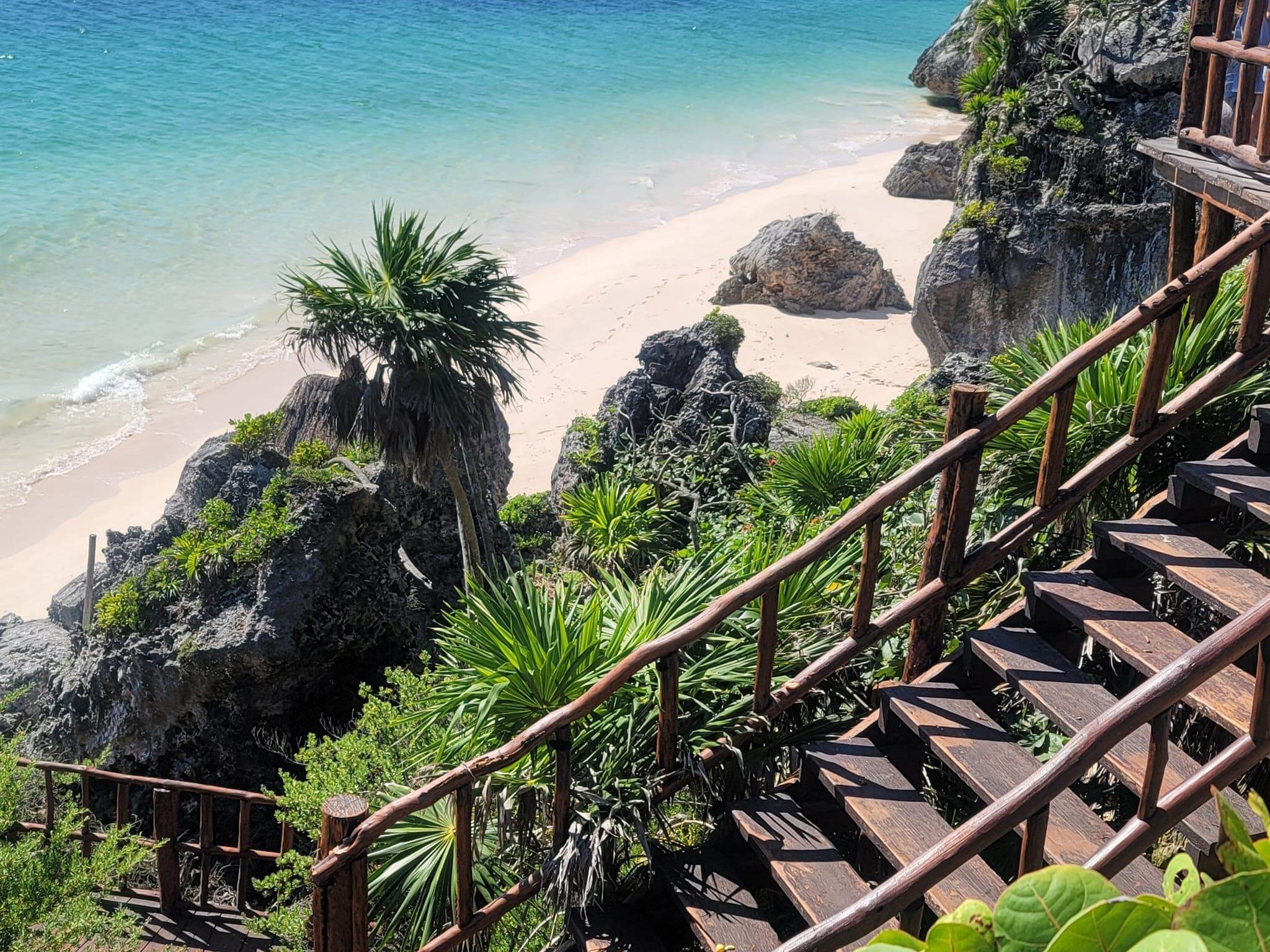 View of a wooden staircase leading down to a pristine white sand beach and calm waters on a sunny day