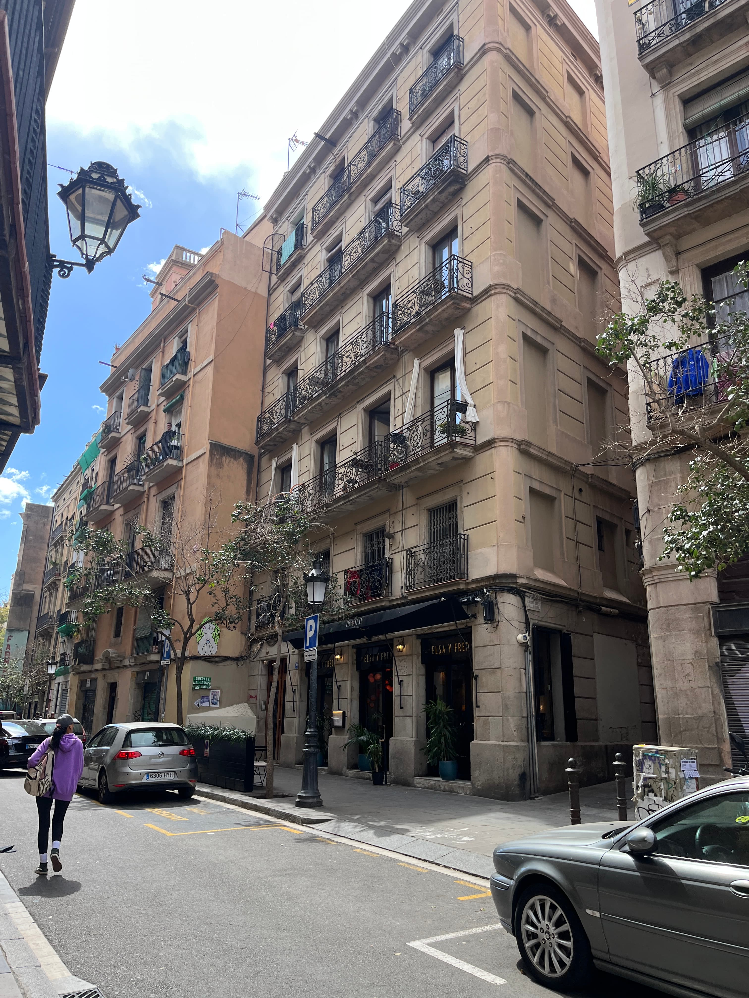 View of a building on a city street with several parked cars and a pedestrian