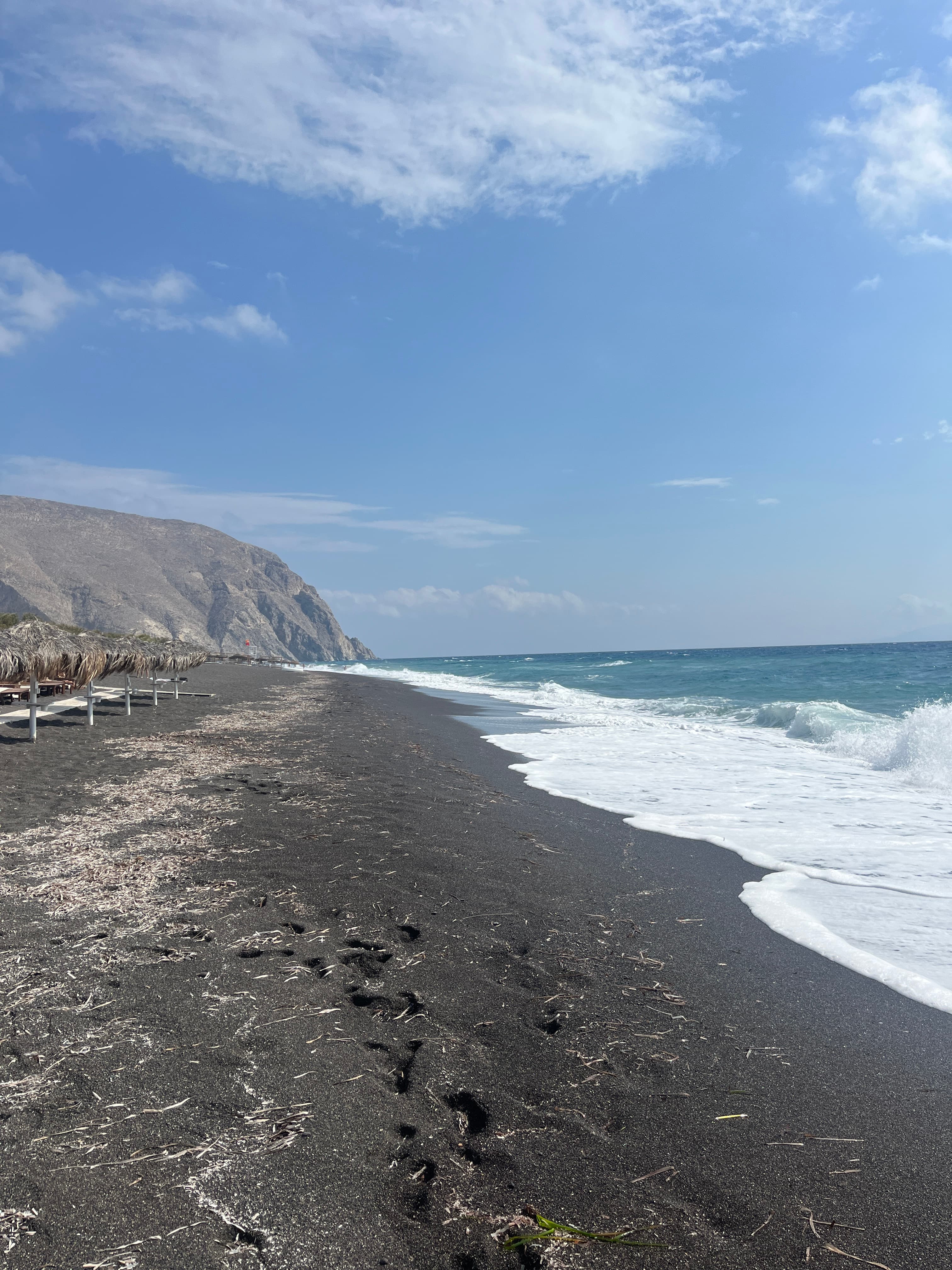 View of a beautiful empty black sand beach with waves crashing ashore on a sunny day