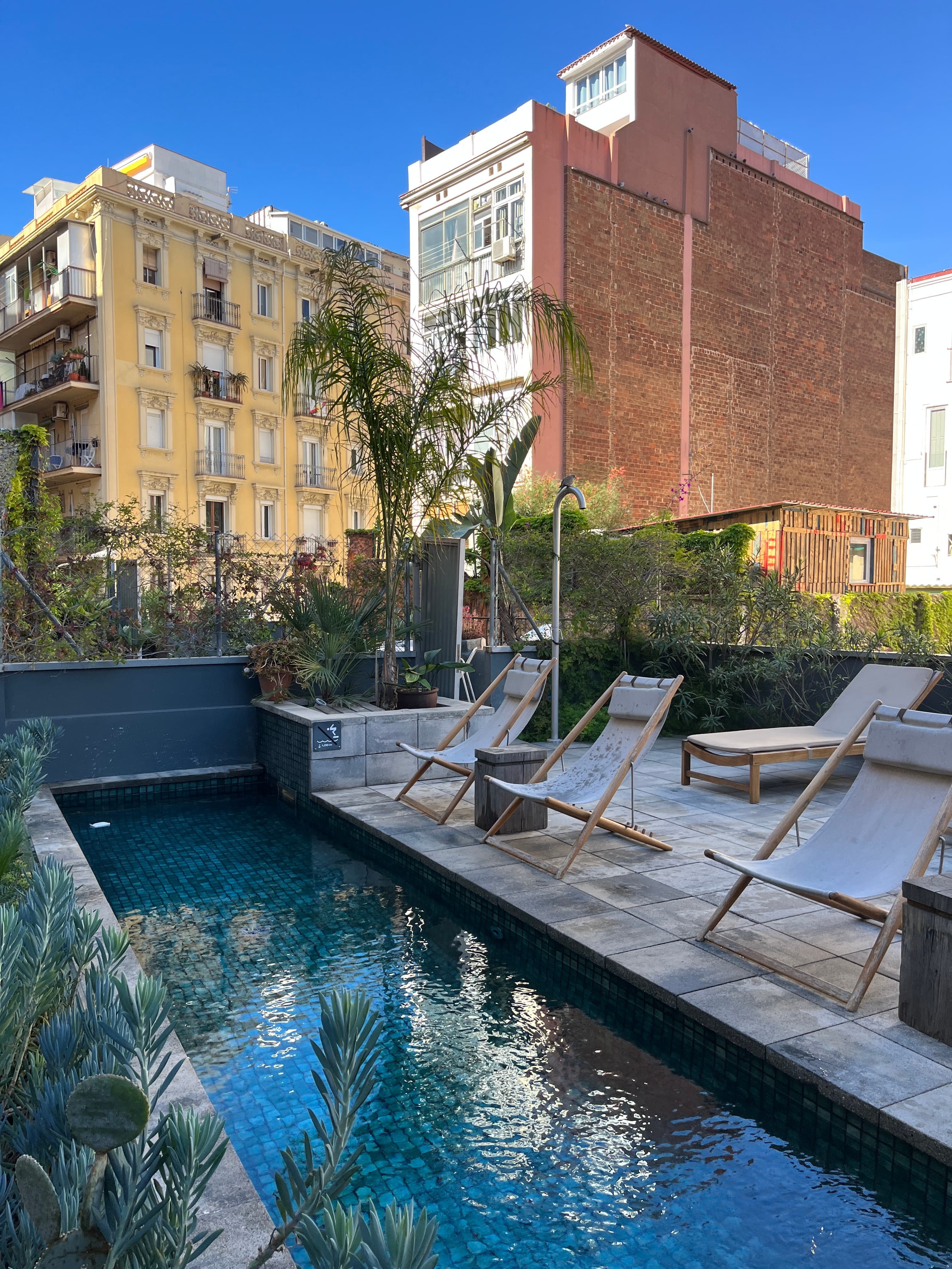 View of a small rooftop pool with lounge chairs and city buildings visible behind it