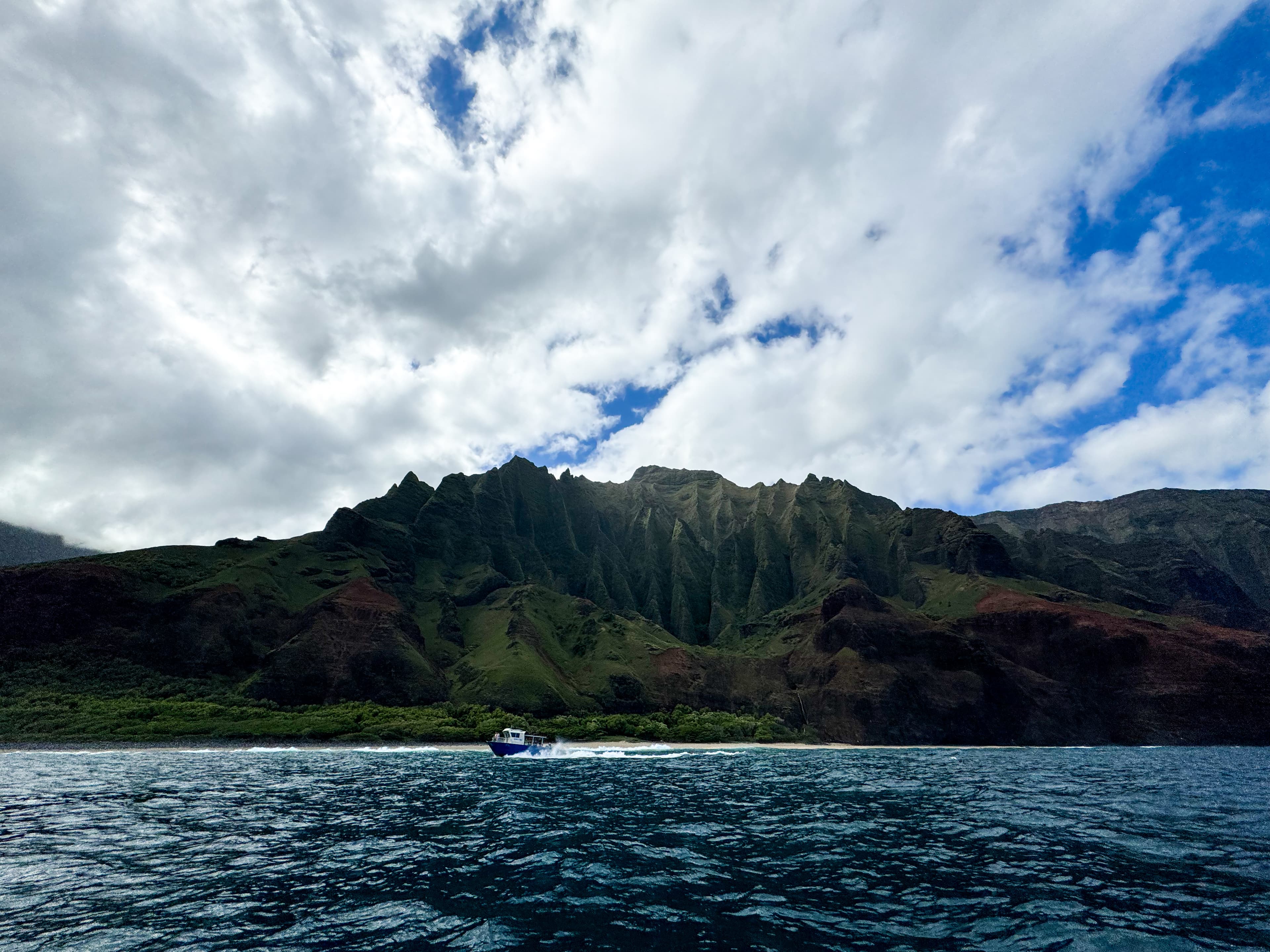A boat sails near mountain peaks during the daytime.