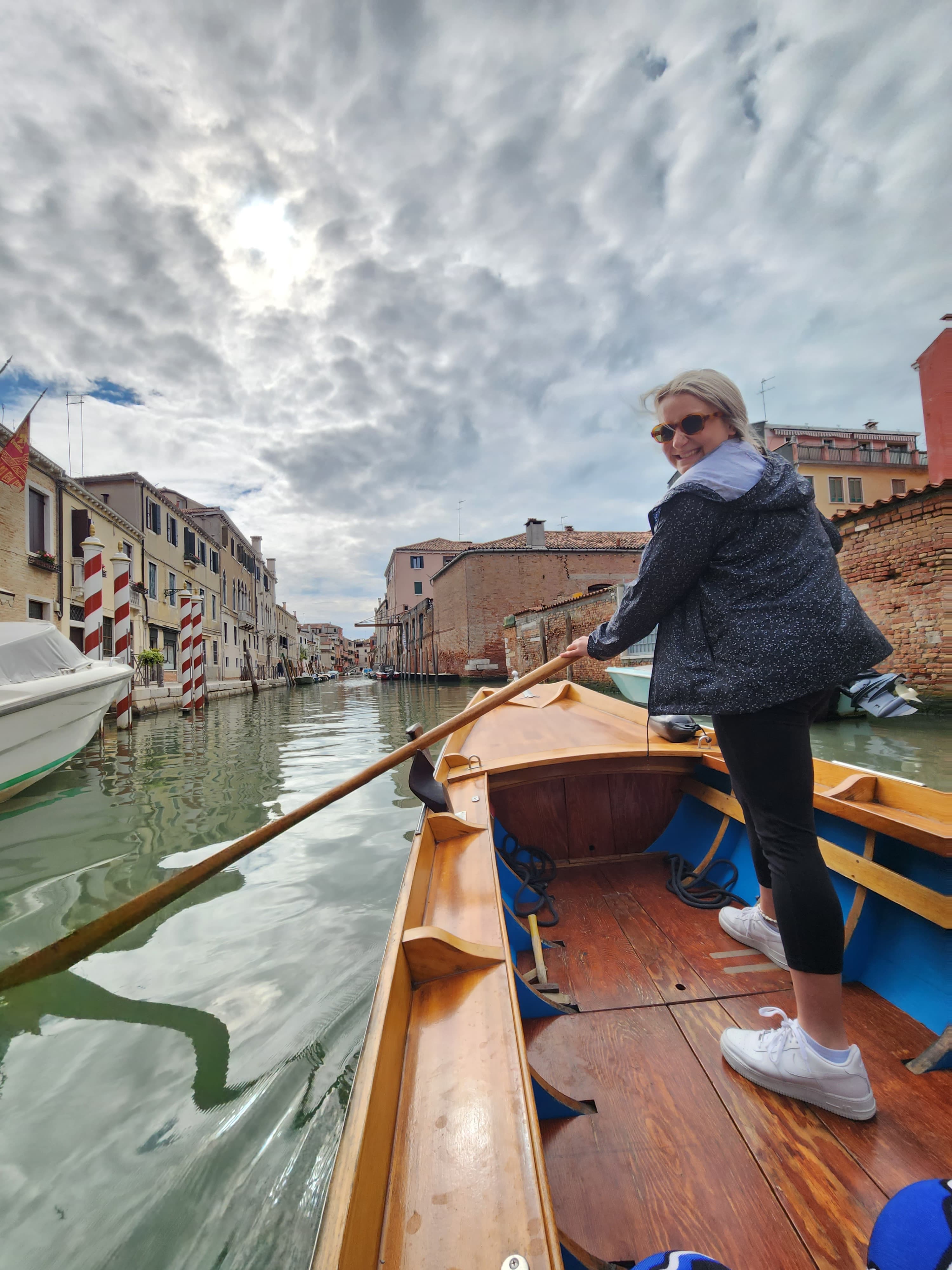 A woman rows a boat down a serene canal surrounded by lush greenery.