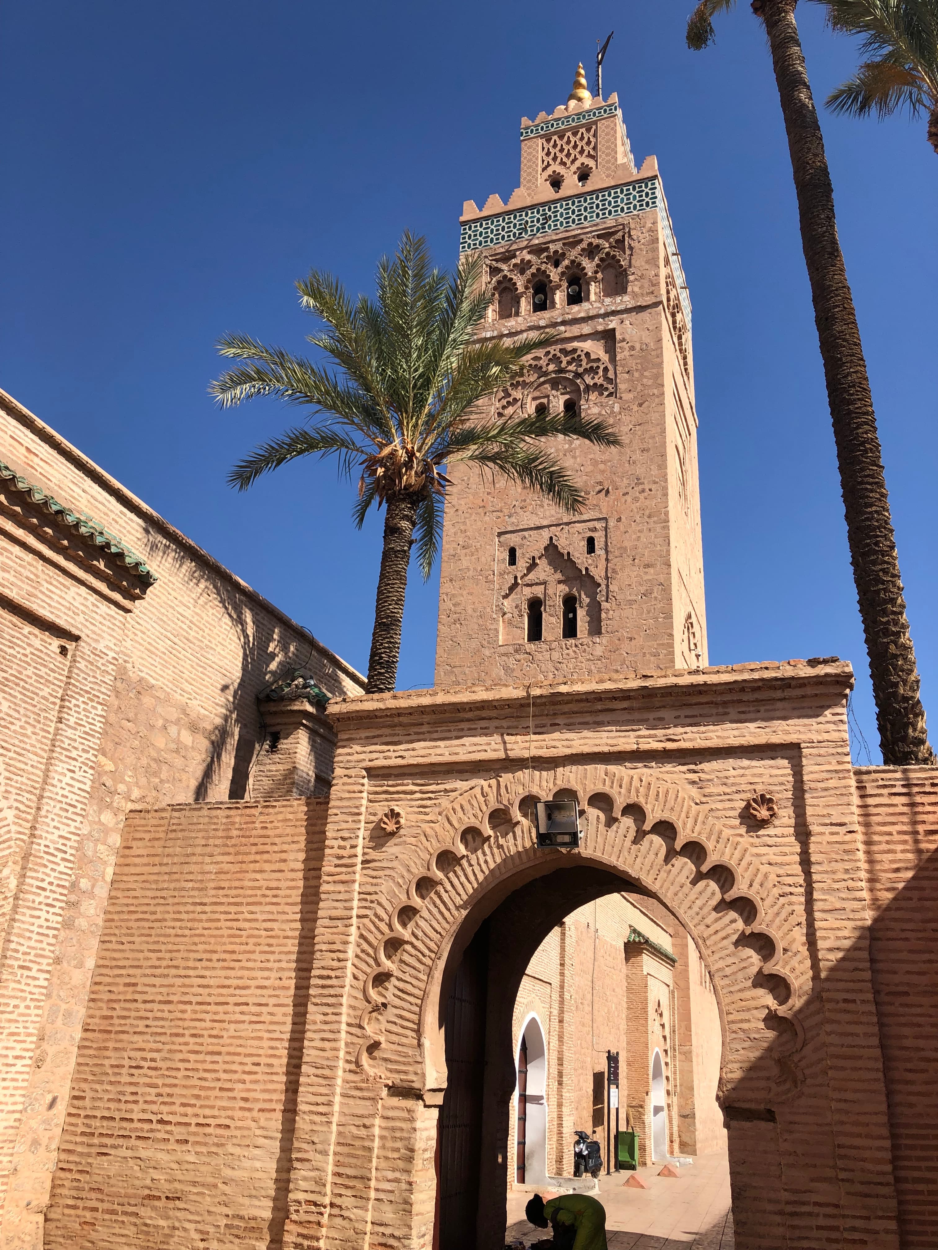 View of an arch and tower with nearby palm trees against blue skies