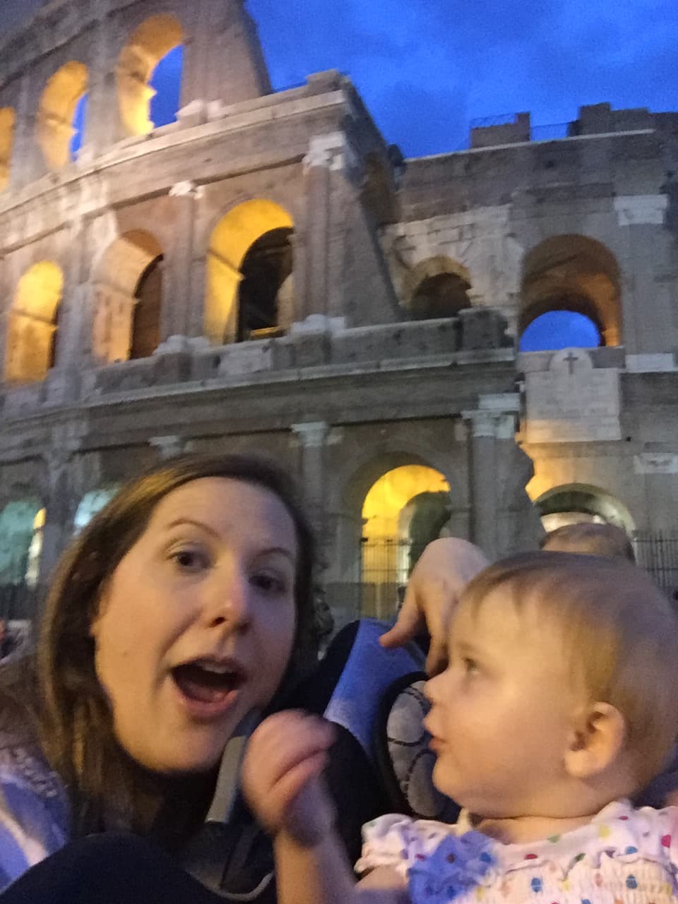 Tammy taking a selfie with a young baby in front of the Colosseum at night