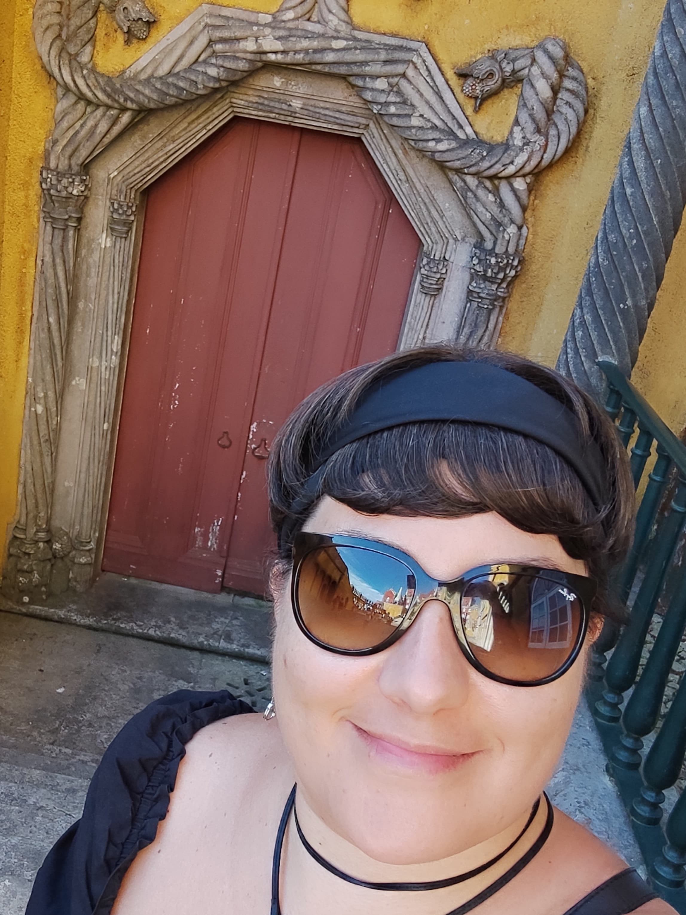 Advisor wearing sunglasses taking a selfie in front of a red wooden door and yellow wall