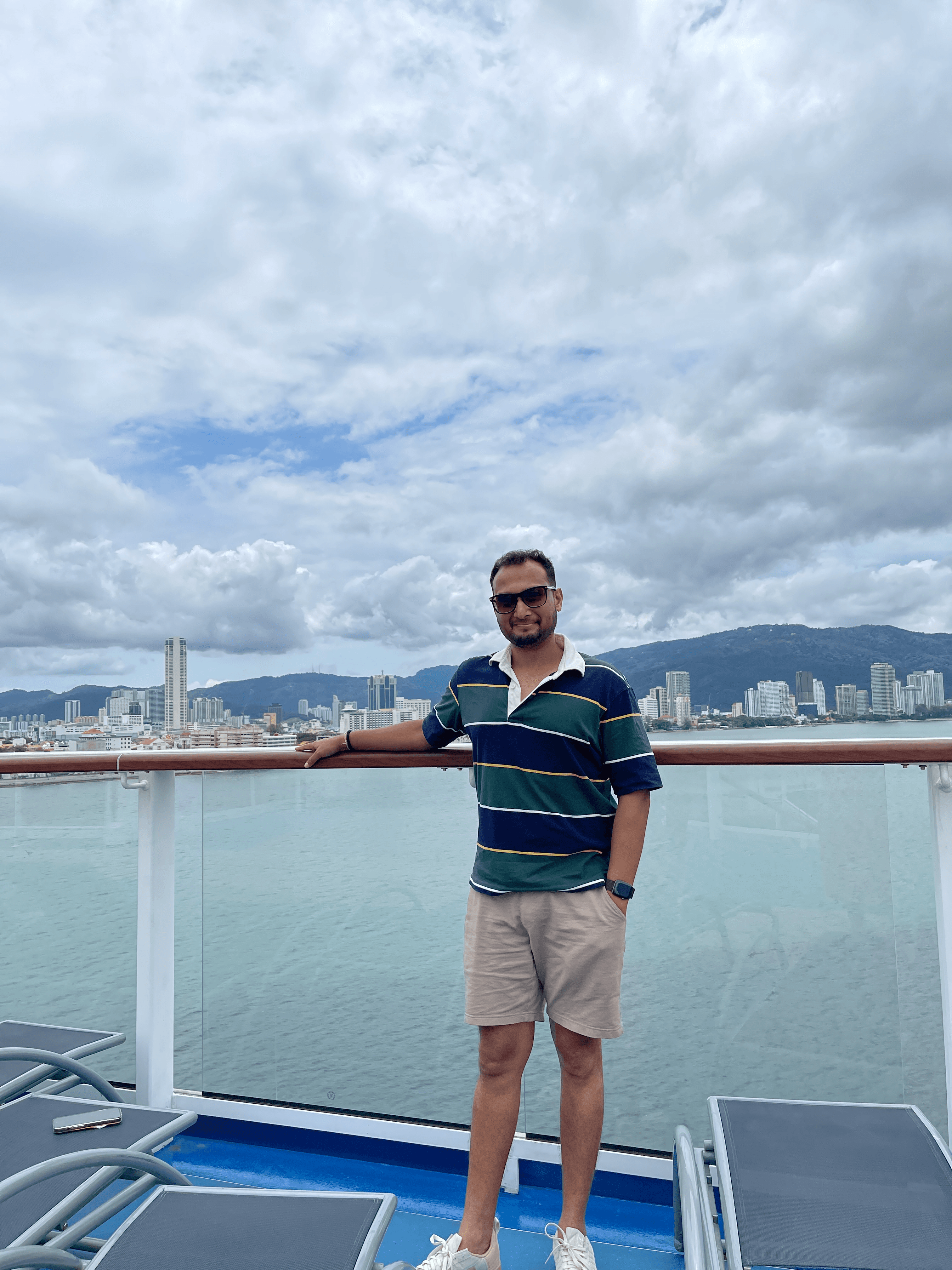 Advisor in a striped shirt resting his arm on a glass railing on a boat with a cityscape visible in the distance