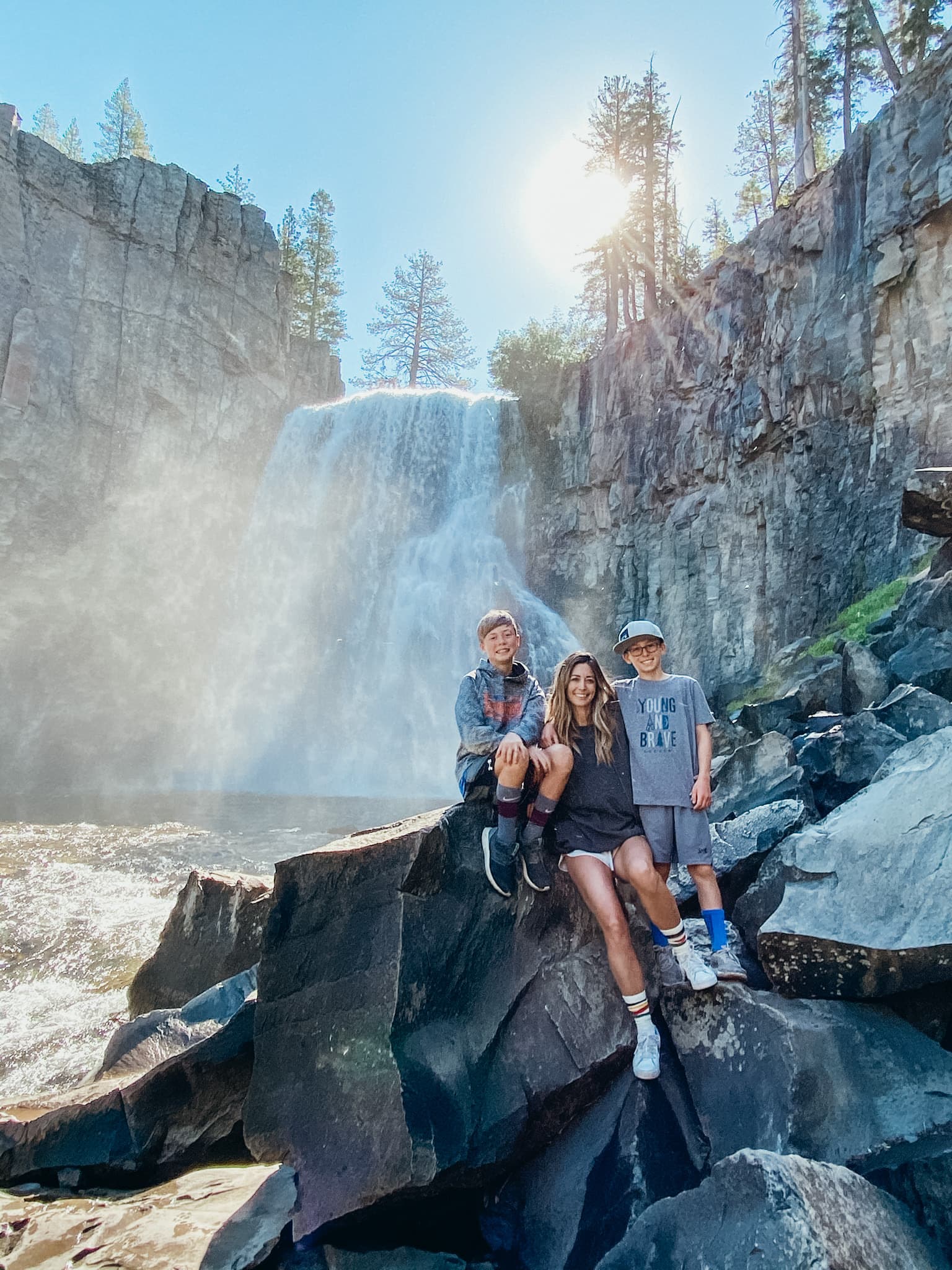 Jill and two young boys seated on a rock in front of a beautiful water on a sunny day