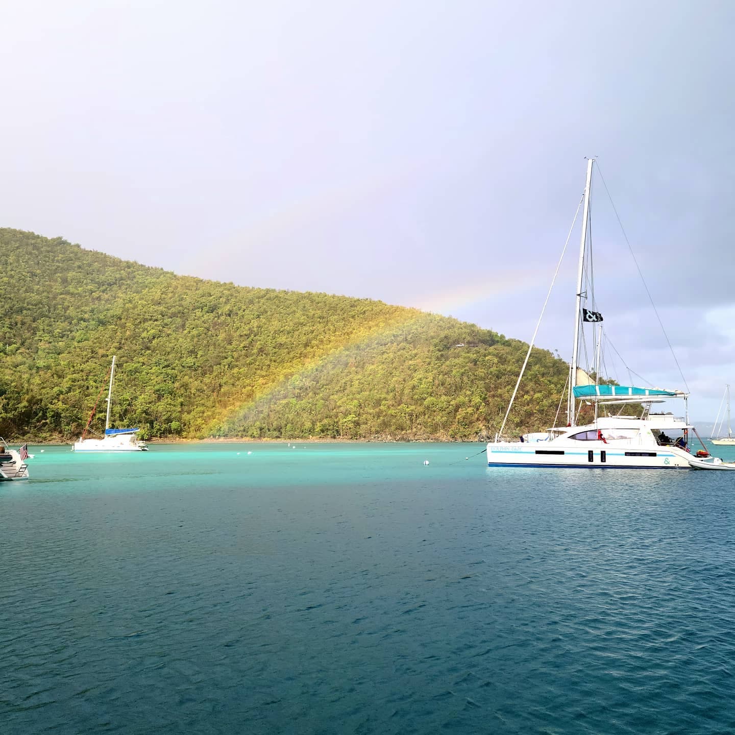View of a boat on a lake with a hill in the background, with a rainbow in the sky.