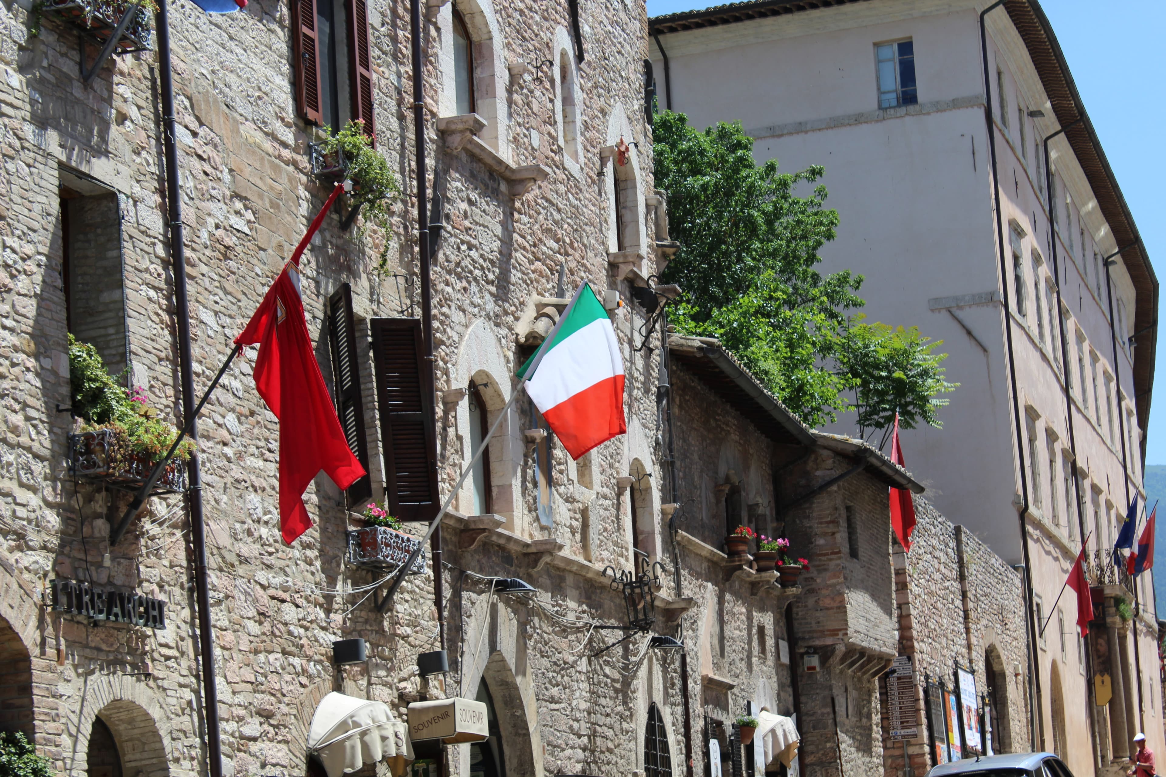 A view of a town in Italy on a sunny day with flags outside.