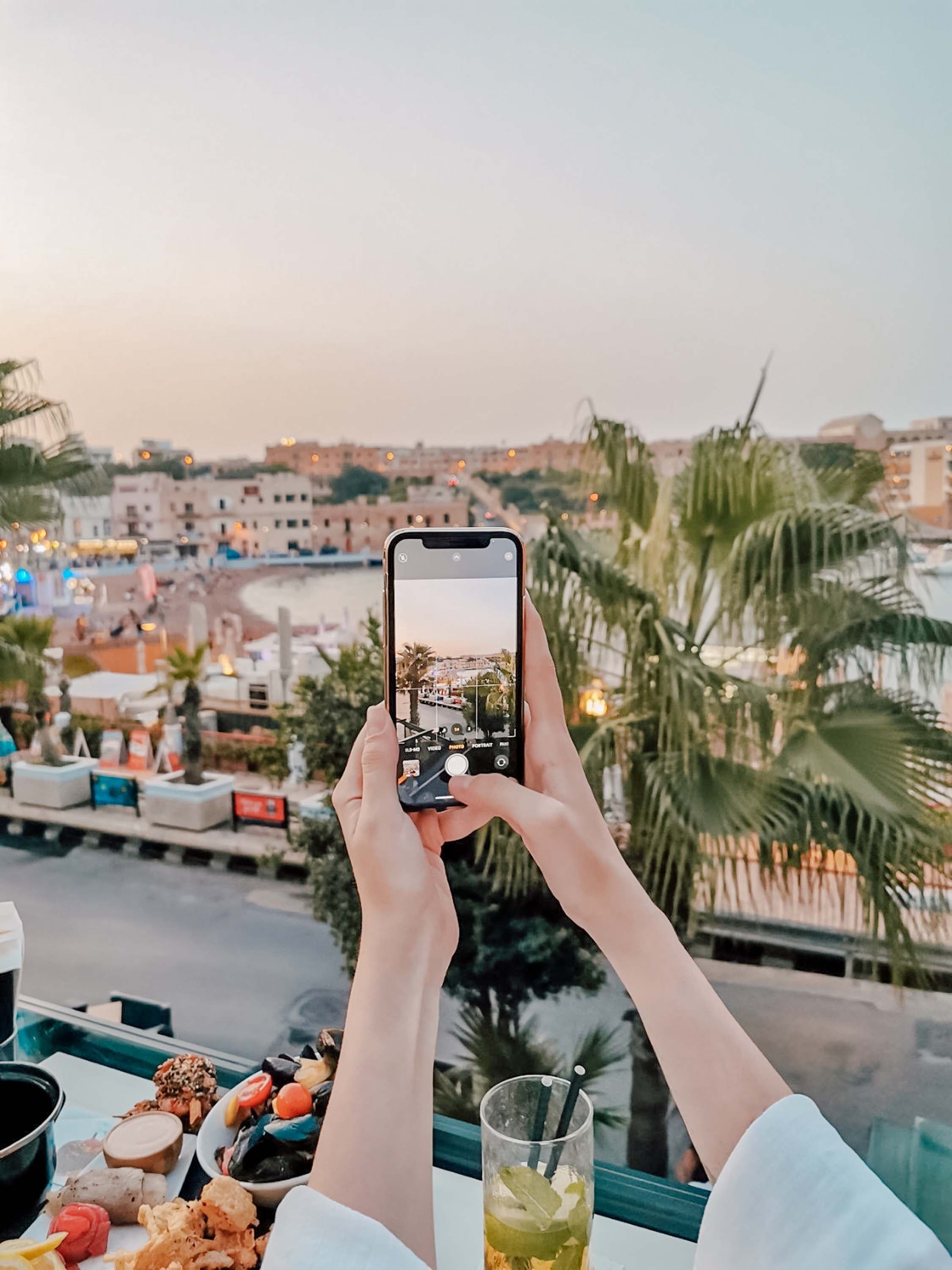 Someone taking a picture with palm trees and a body of water in the distance.
