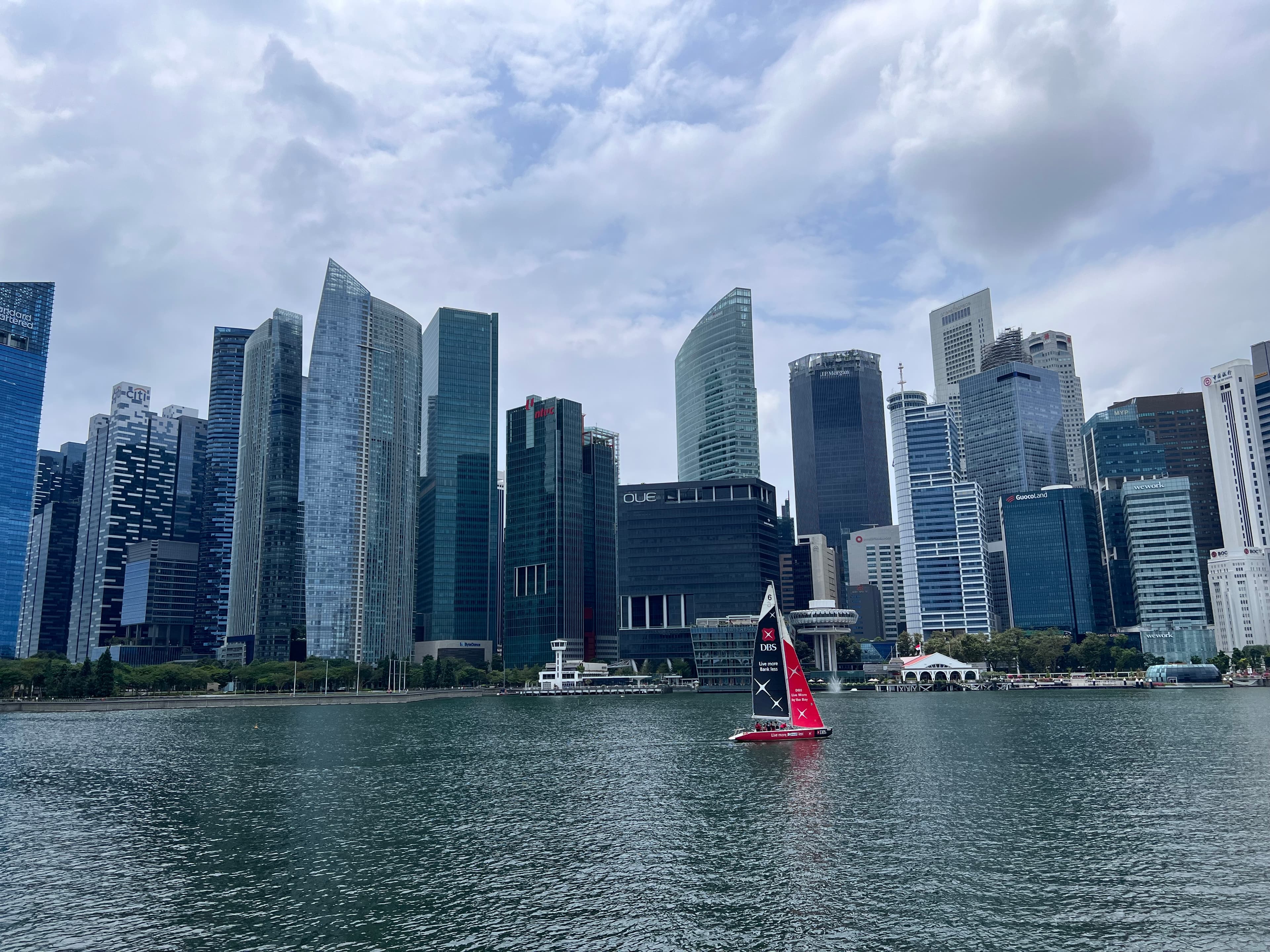 Skyscrapers reach toward the sky as water laps the shore on a cloudy day.