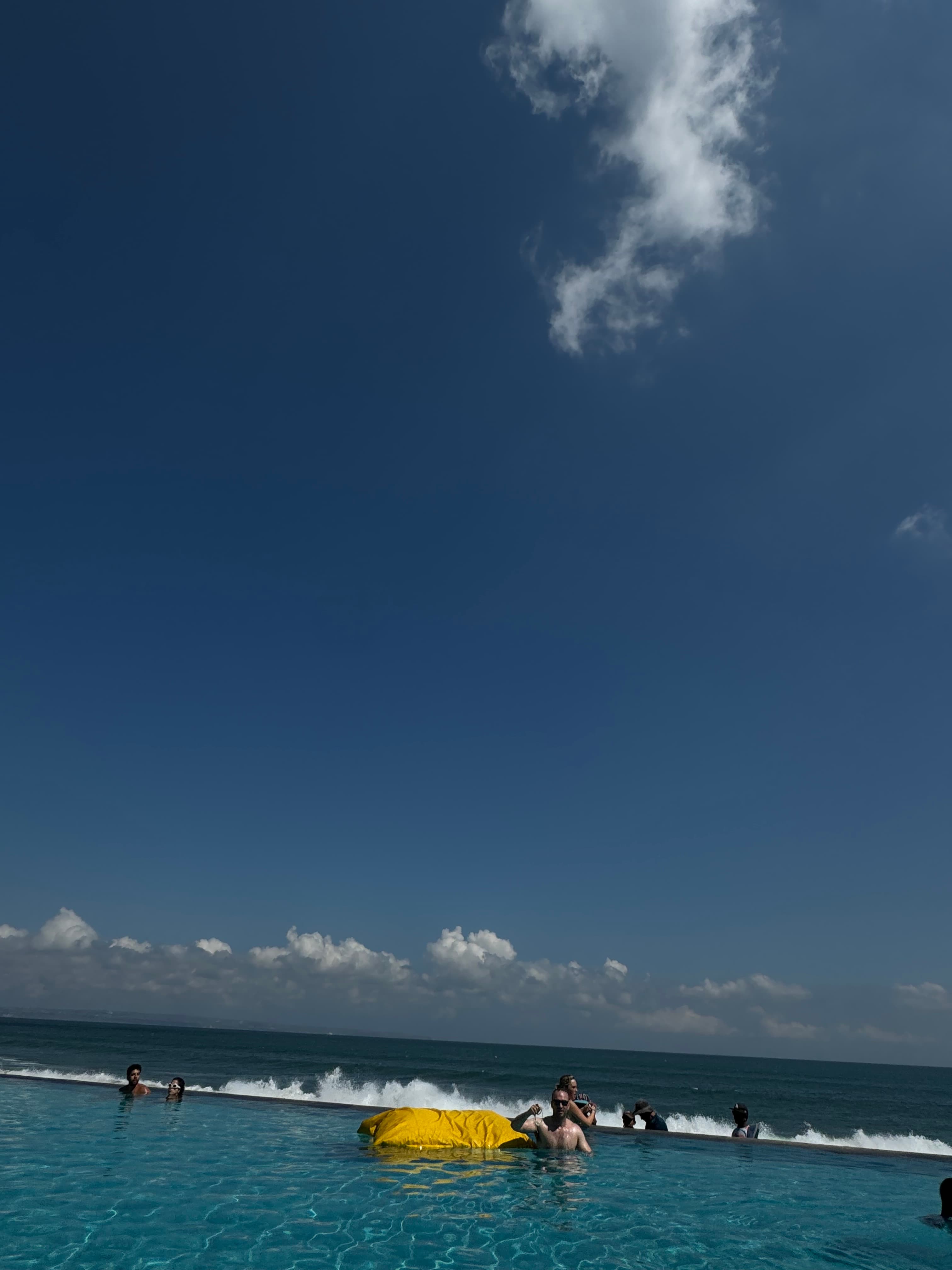 Beach goers wade into the waves as clouds float past on a sunny day.