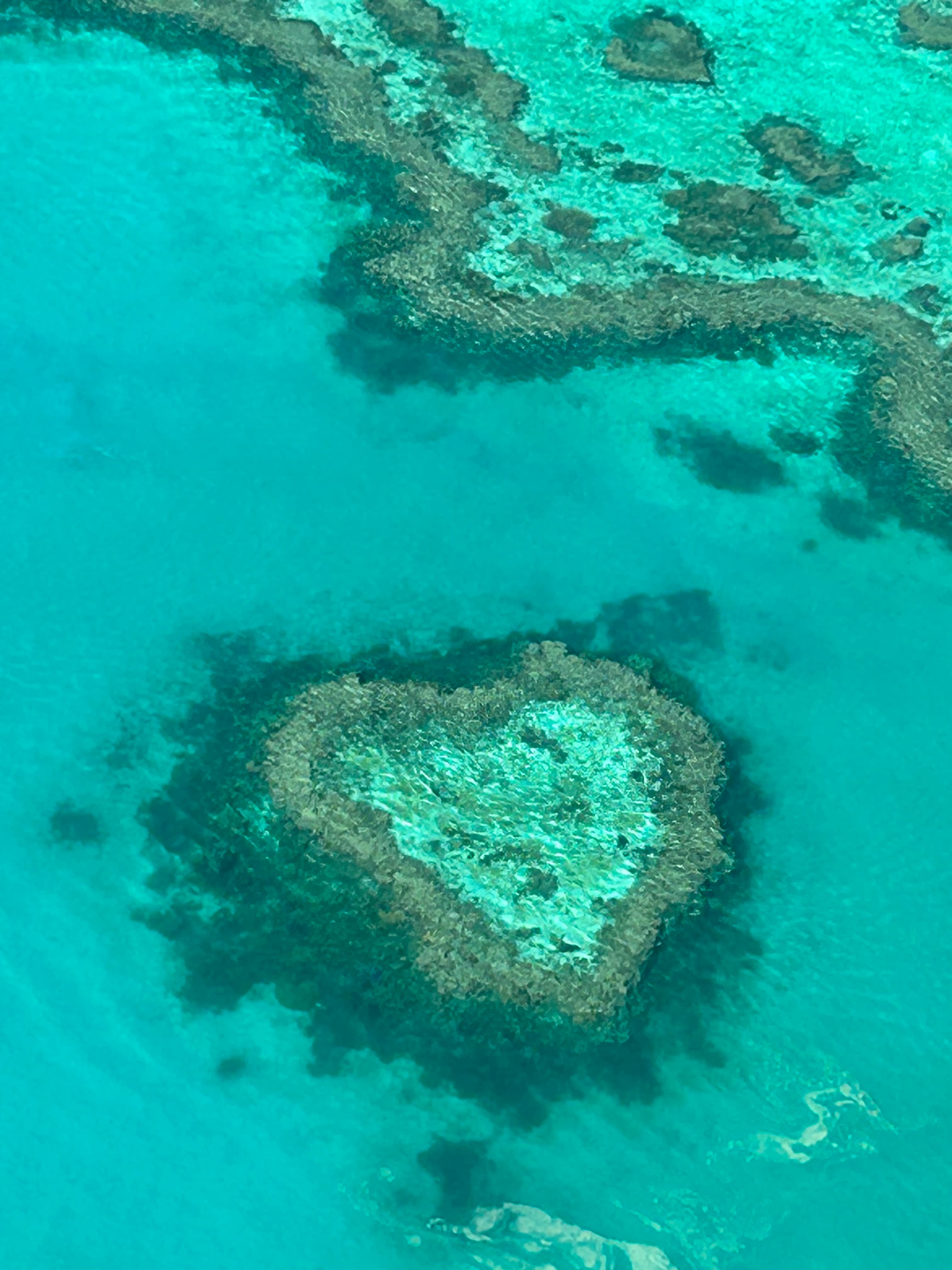 A heart-shaped island is viewed from above as waves lap the shore.