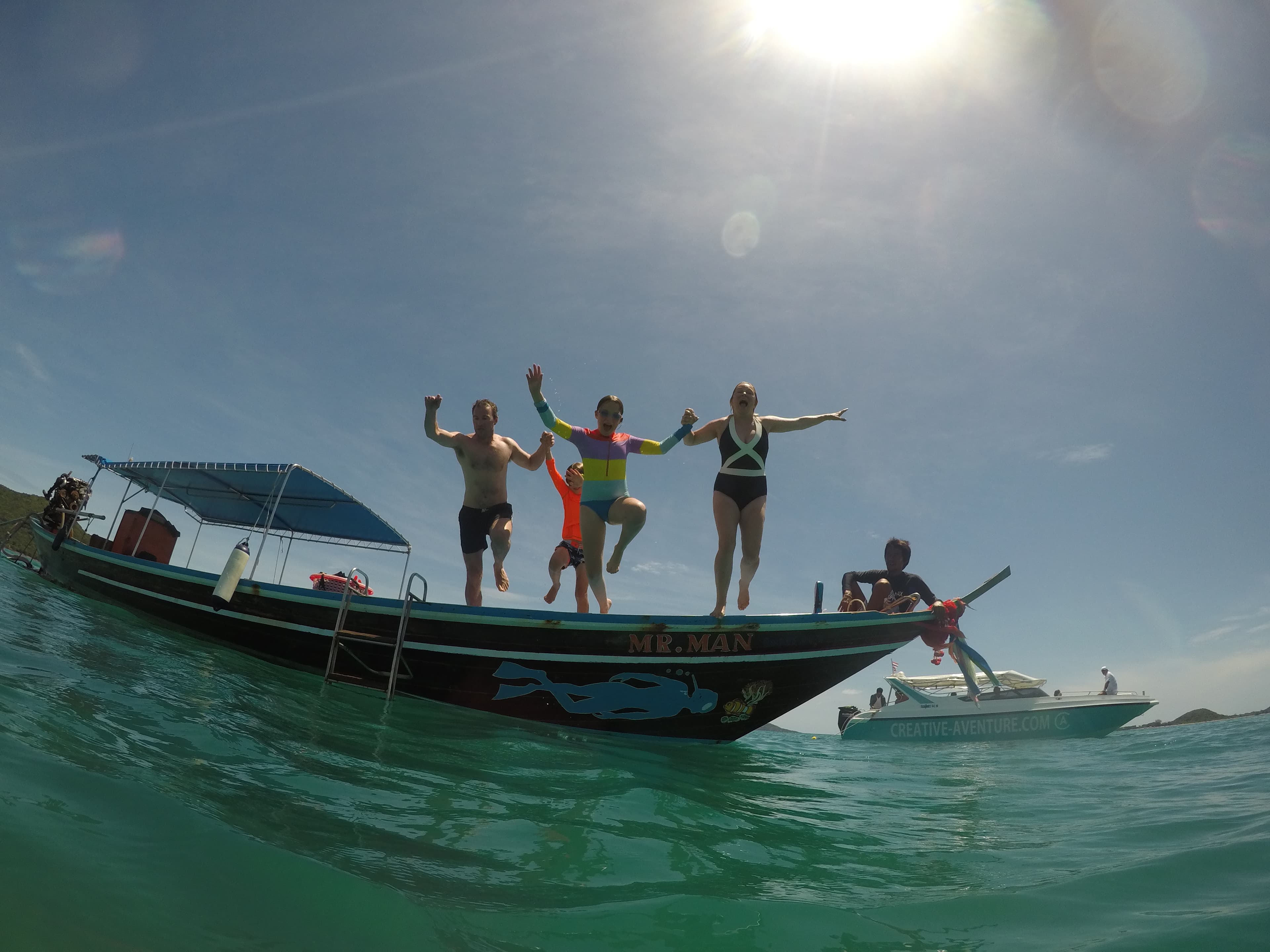 Travelers jump off a boat in crystal-clear water on a sunny day.