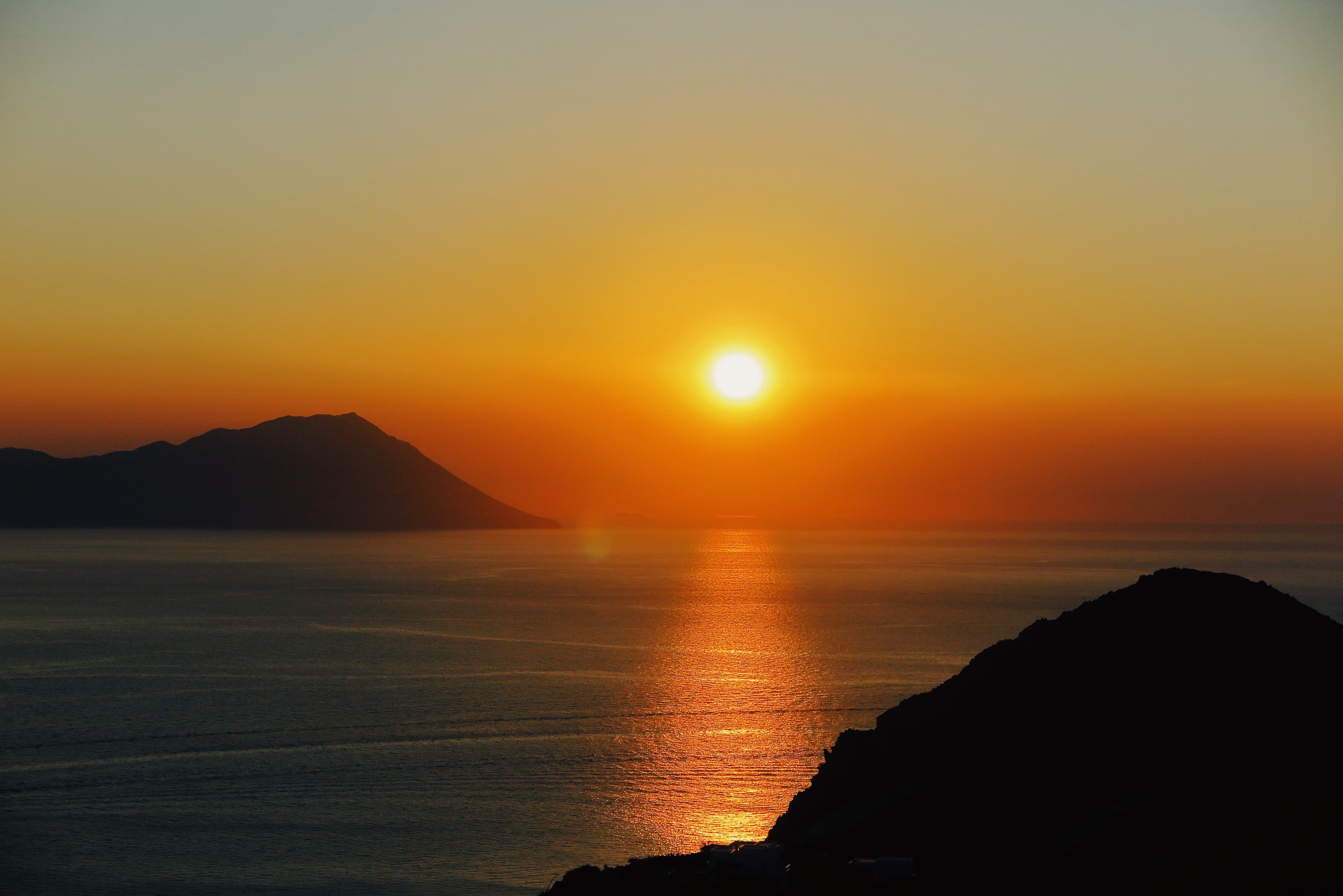 Photo of a sunset over the ocean with mountains in the background.
