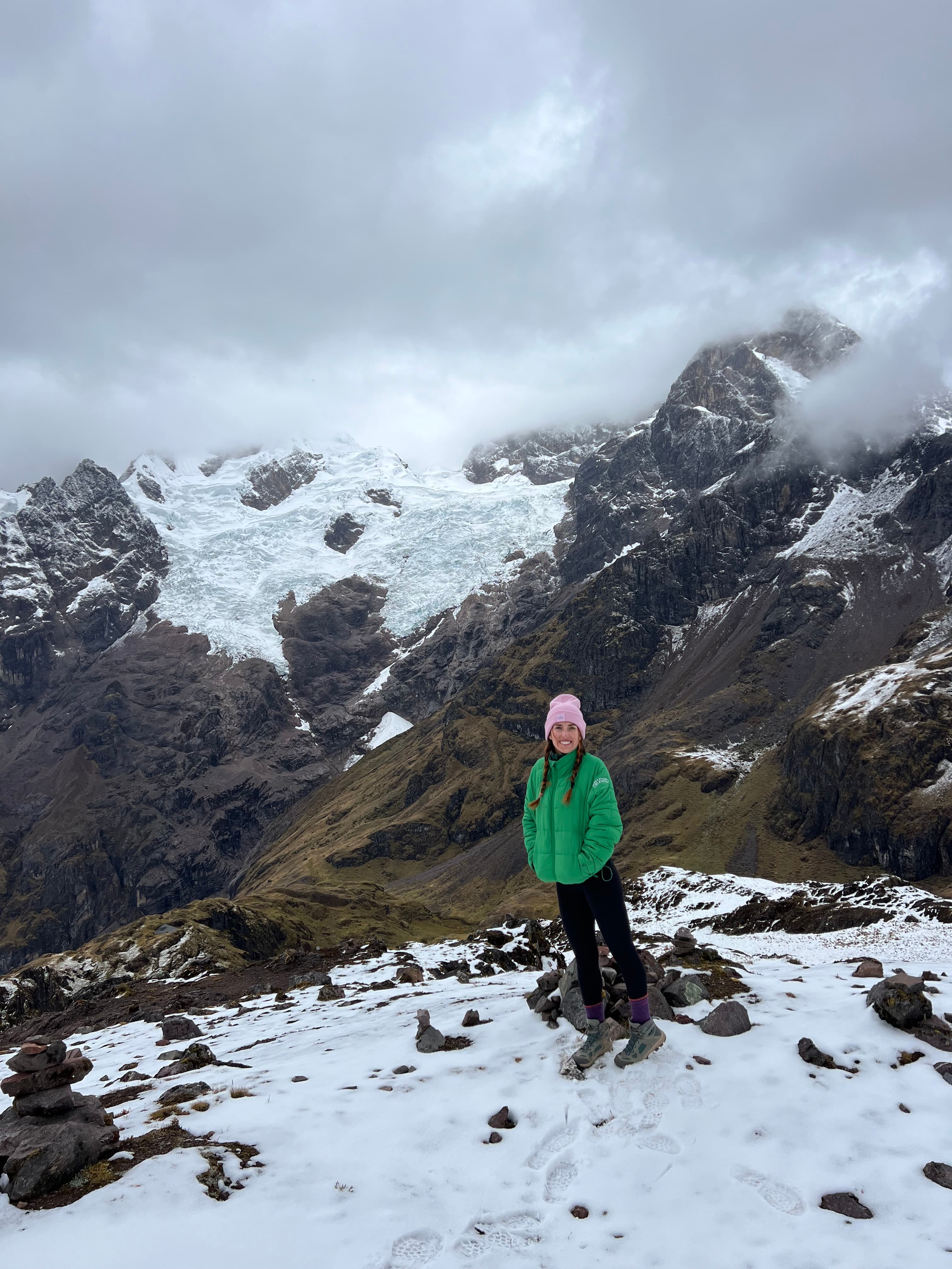 Advisor in a green jacket and winter hat on a hike through a snowy mountain range under cloudy skies