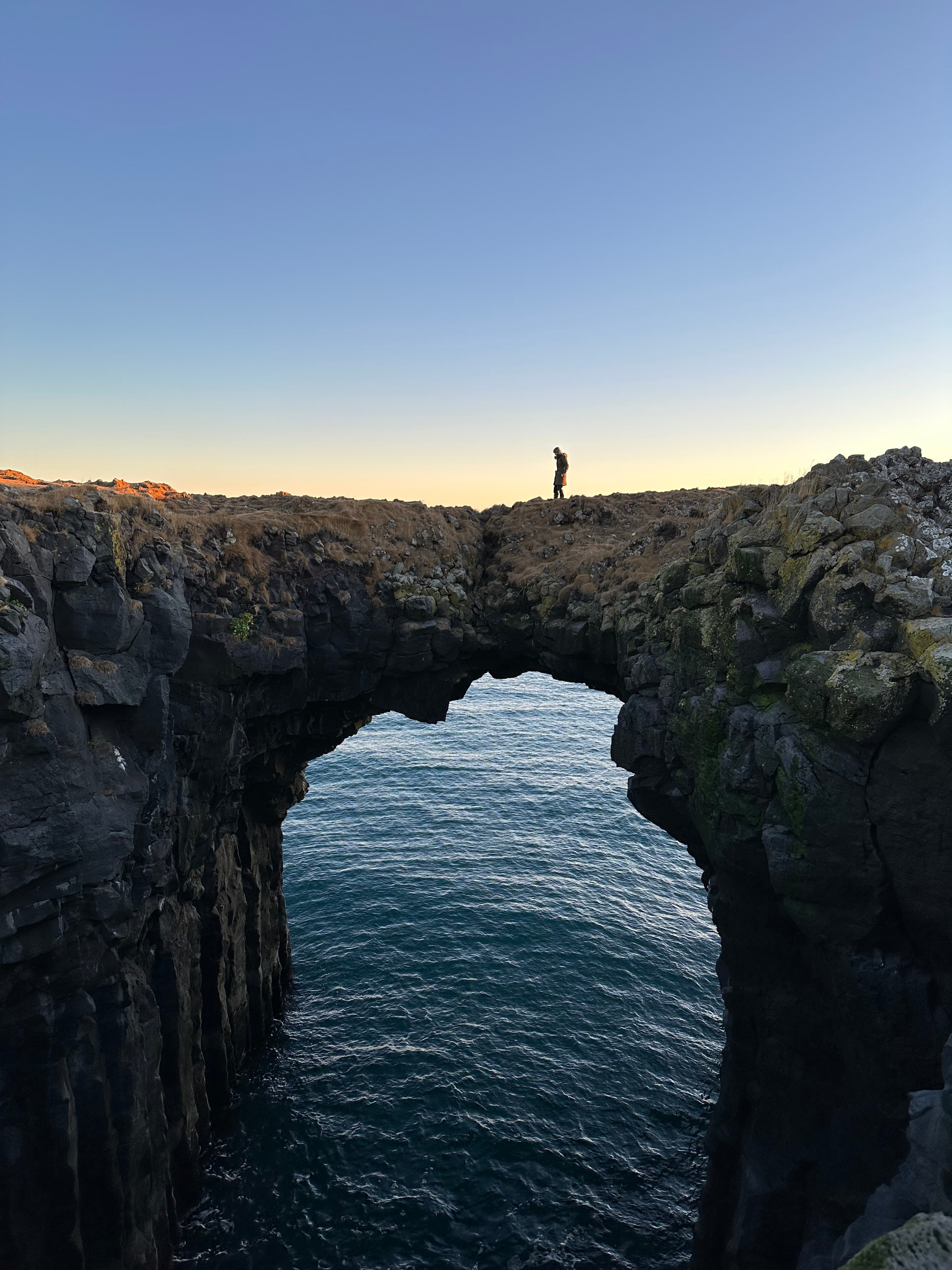 View of a beautiful stone archway over the sea at sunset