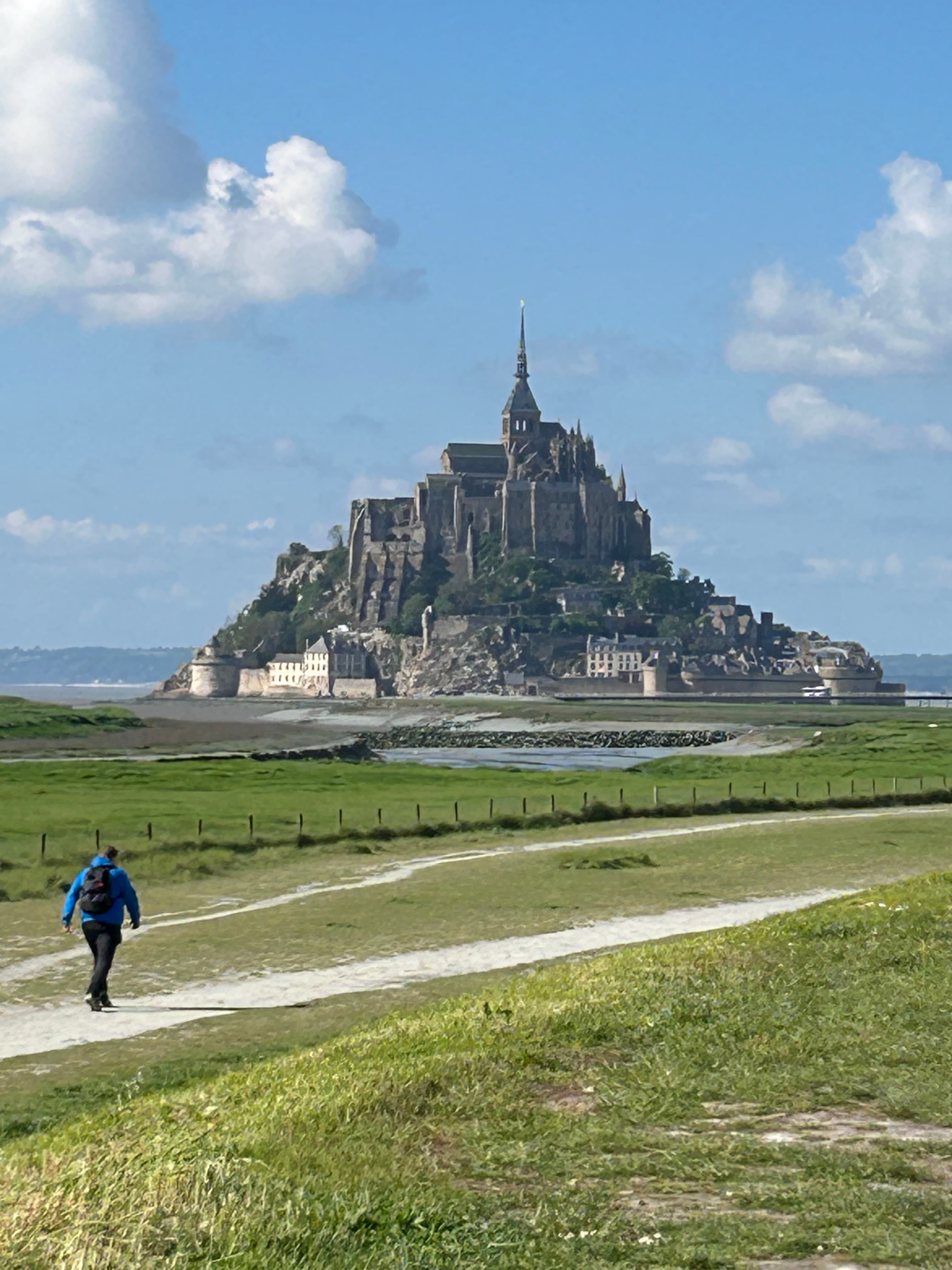 View of one person walking along a path towards Mont Saint-Michel on a sunny day
