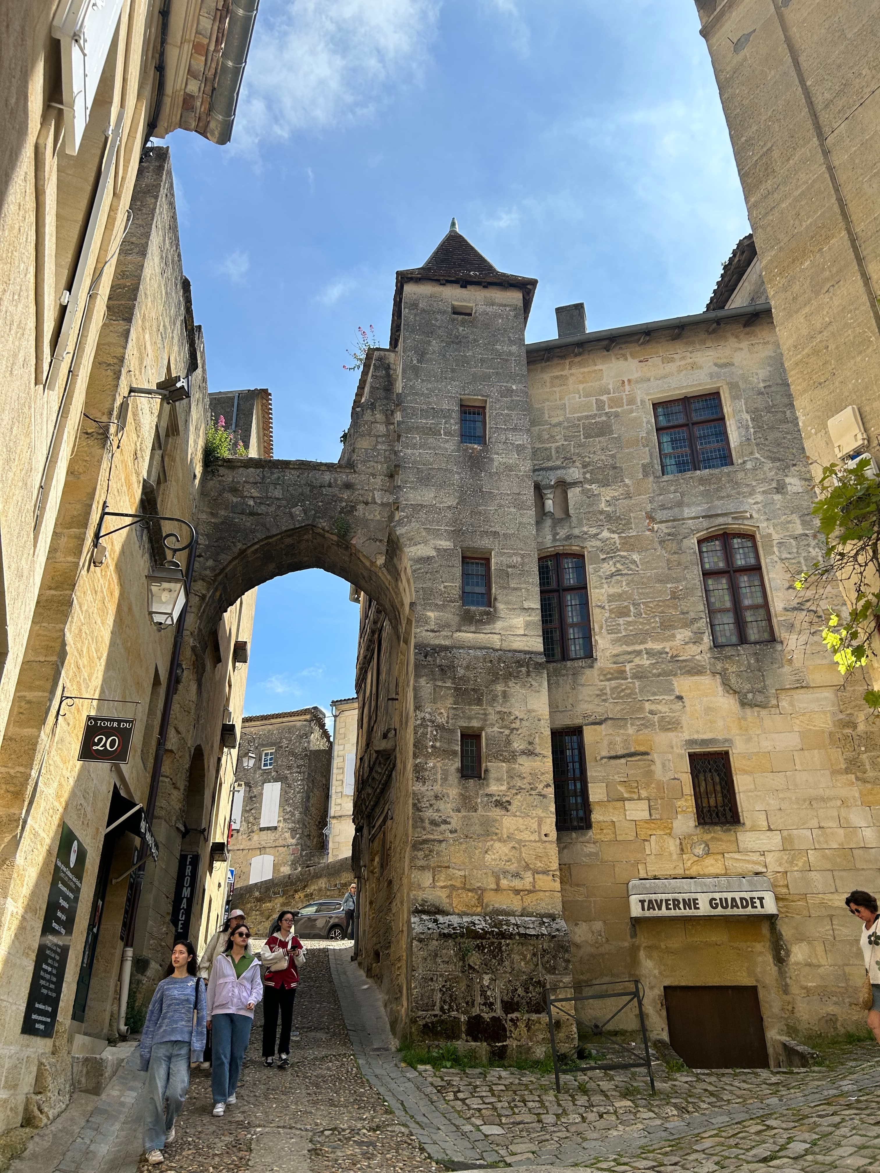 View of old city buildings and a few pedestrians walking beneath an arch on a sunny day