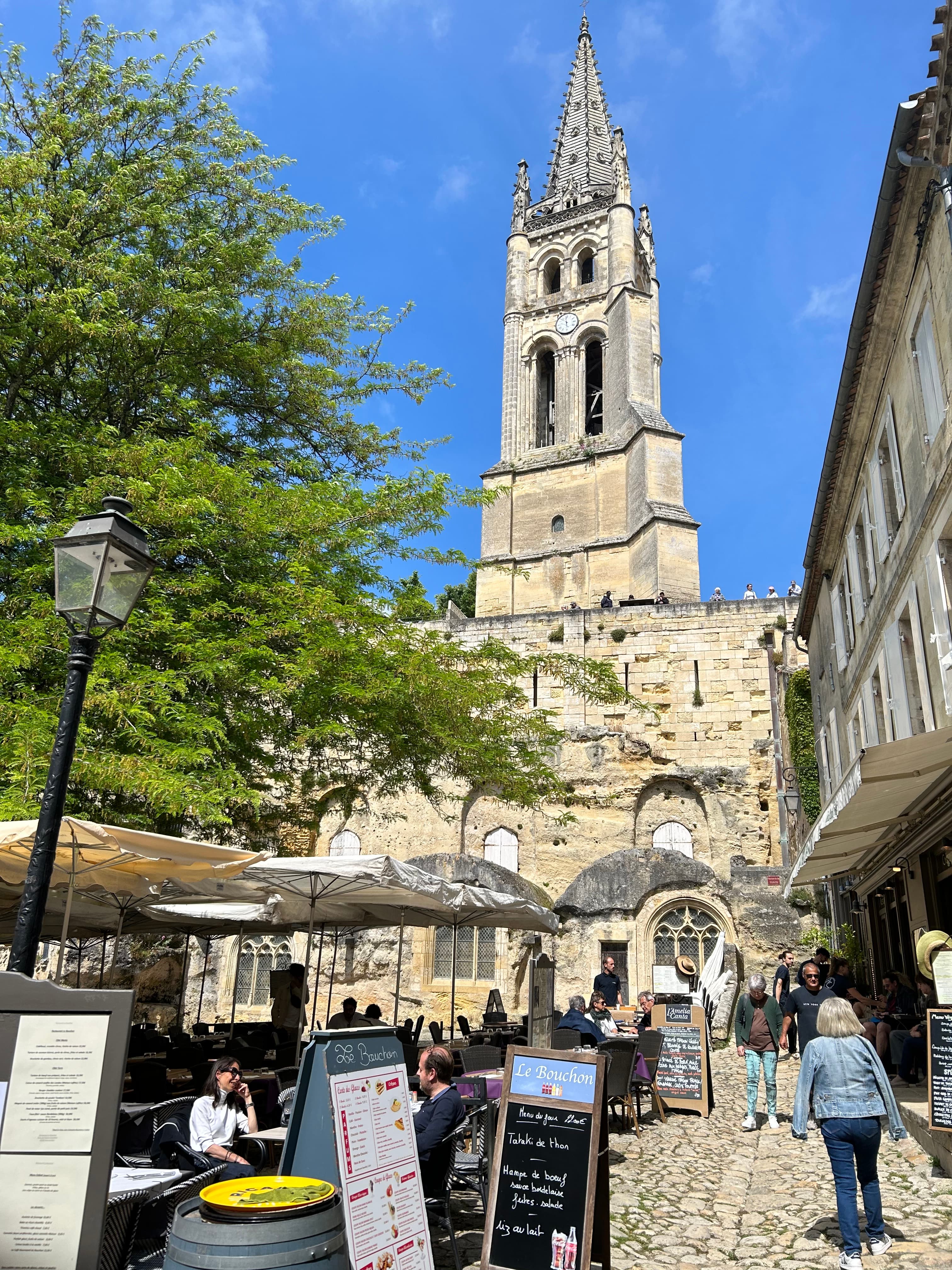 View of an old church tower and outdoor restaurant seating on a cobbled street