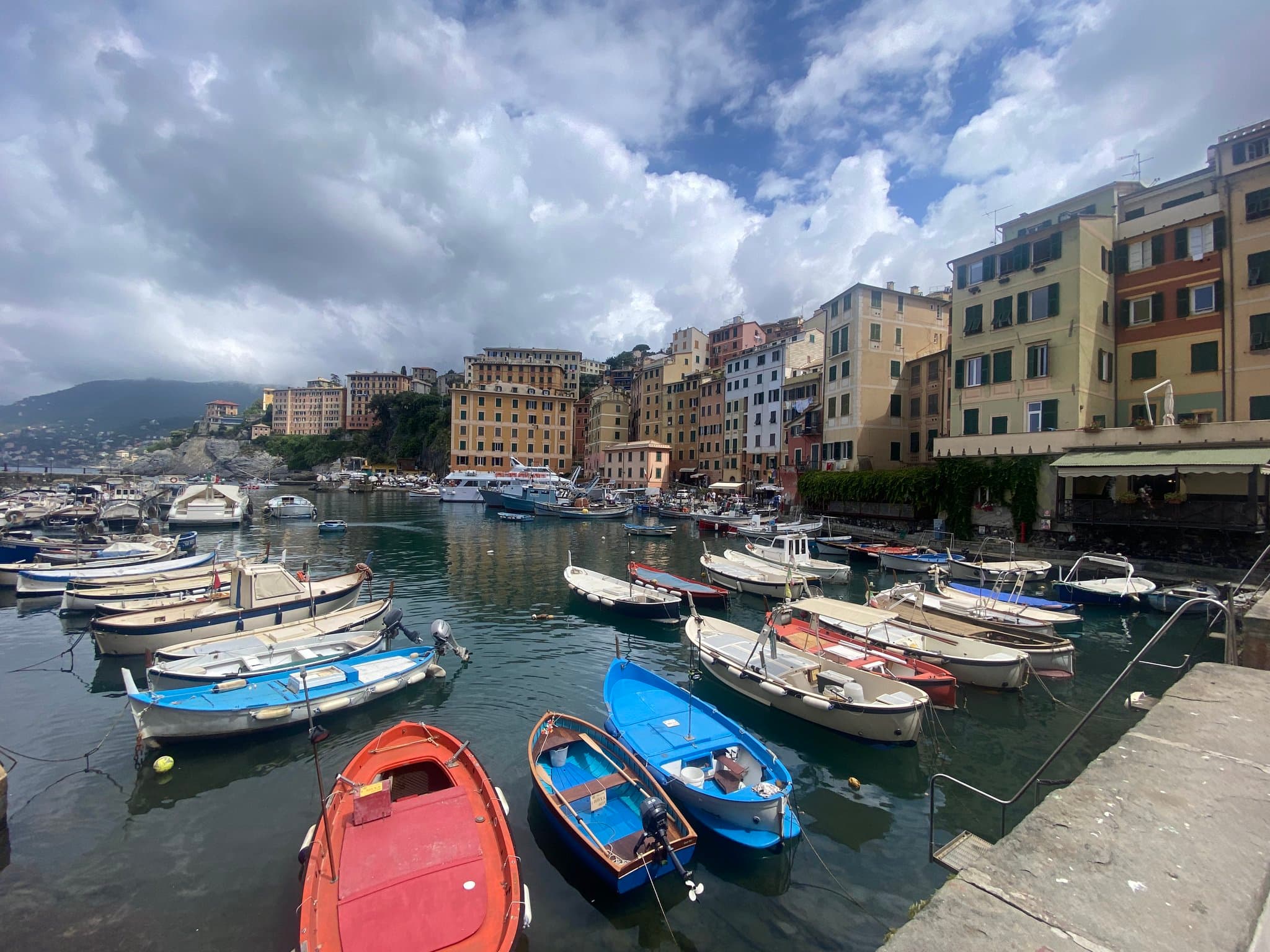 Boats docked along a waterway near colorful city buildings on a cloudy day.