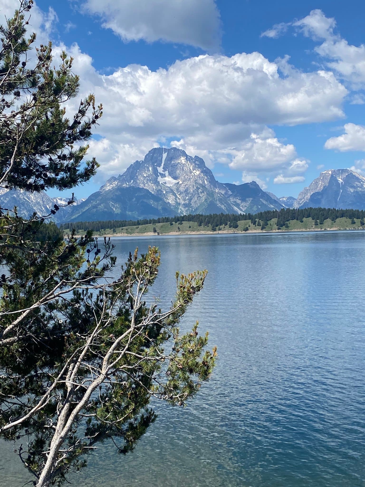 A blue sky with clouds and mountains and lake with green trees.