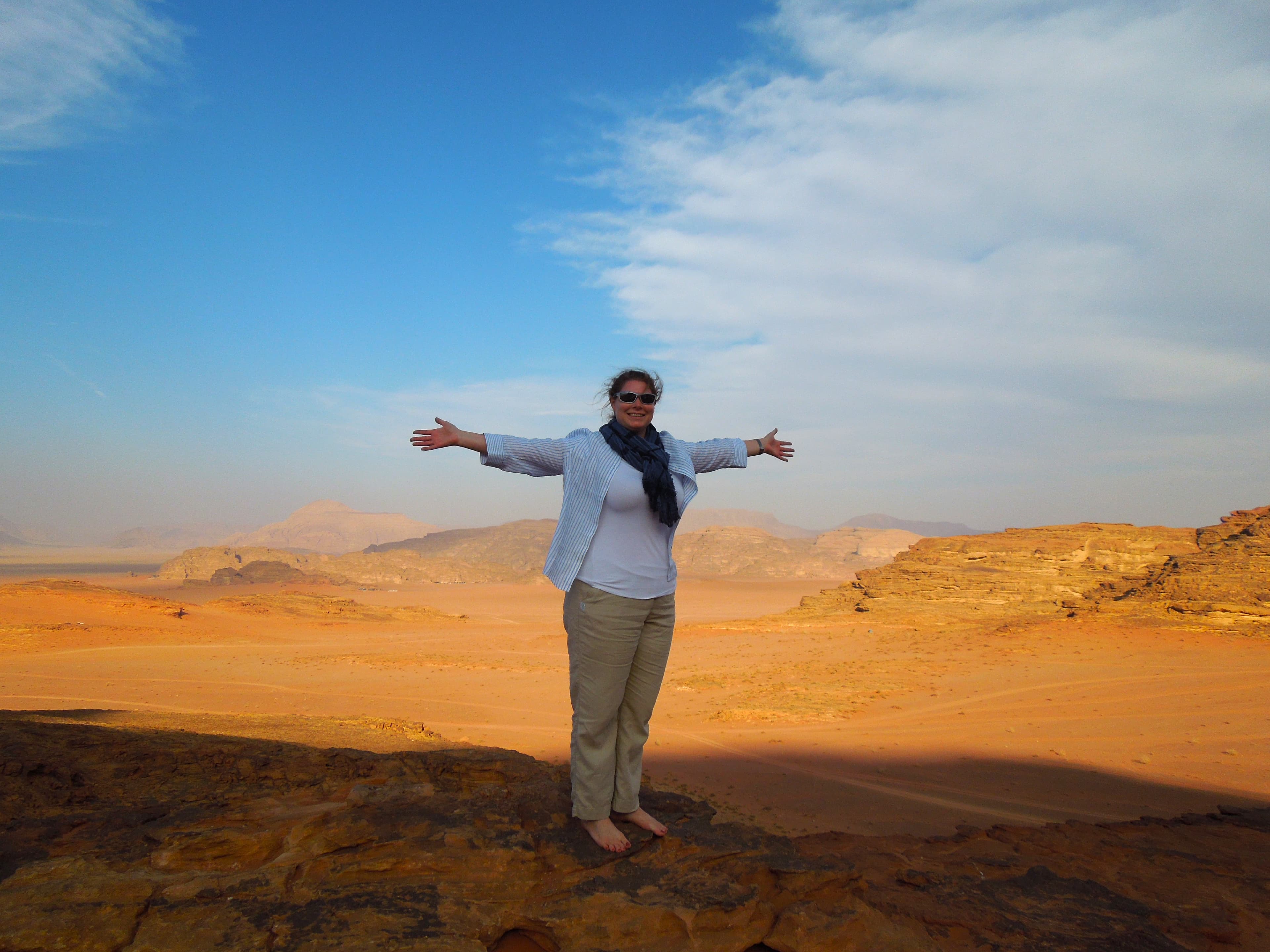 Advisor standing with arms outstretched in the vast Wadi Rum desert under sunny skies