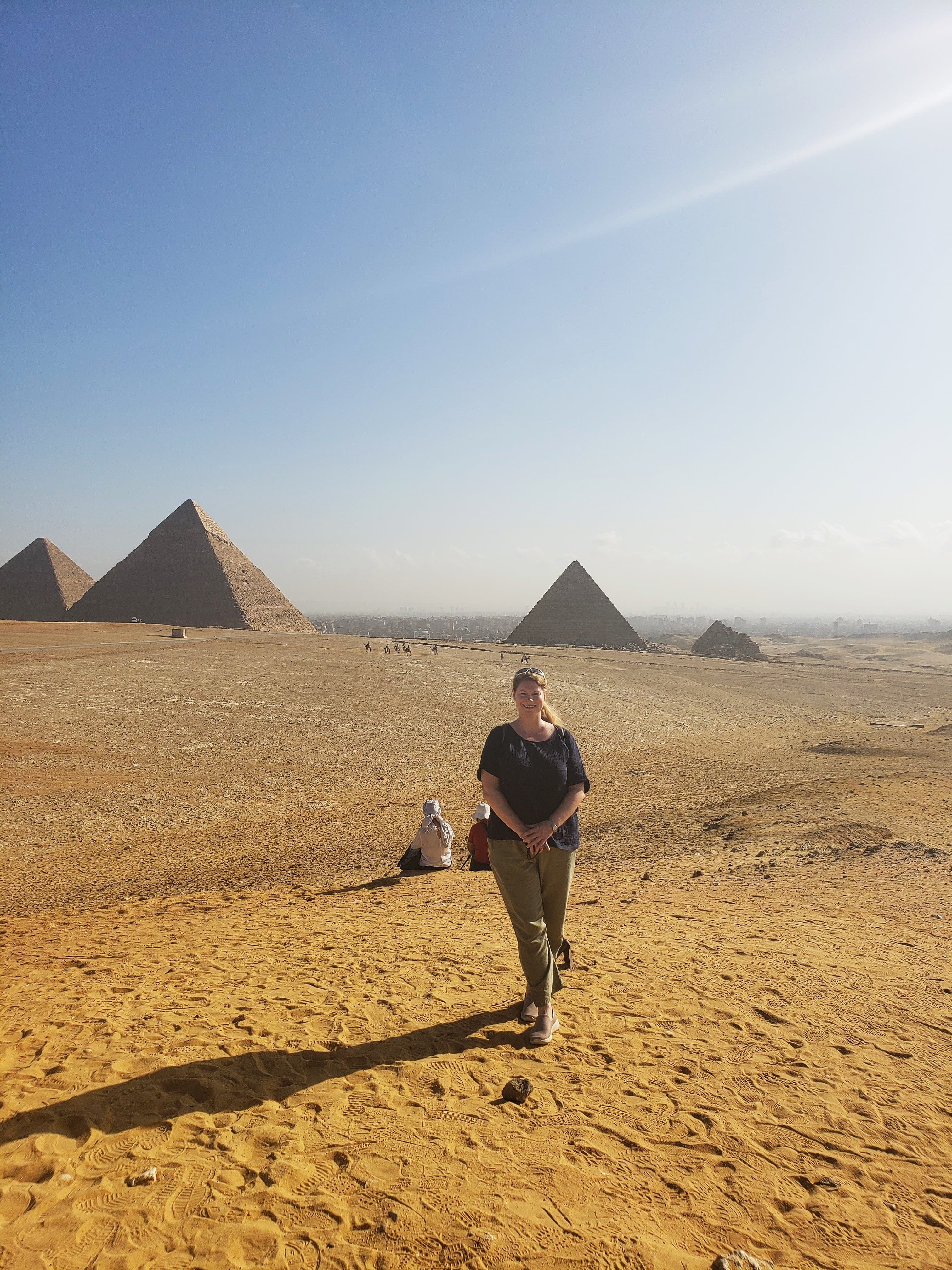 Advisor walking through a desert landscape with the pyramids of Giza visible behind her on a sunny day