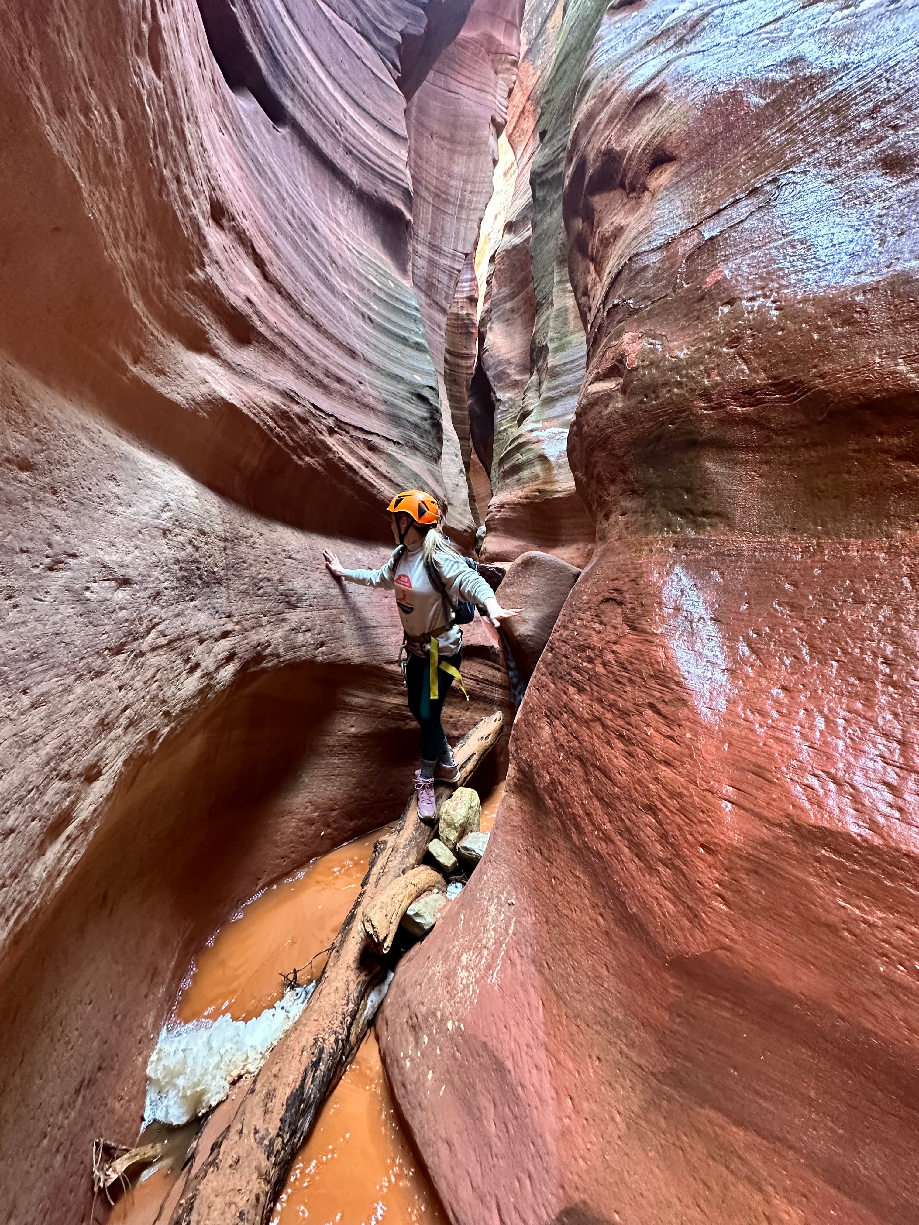 Advisor in climbing gear seen in a crevice of two large red rock formations