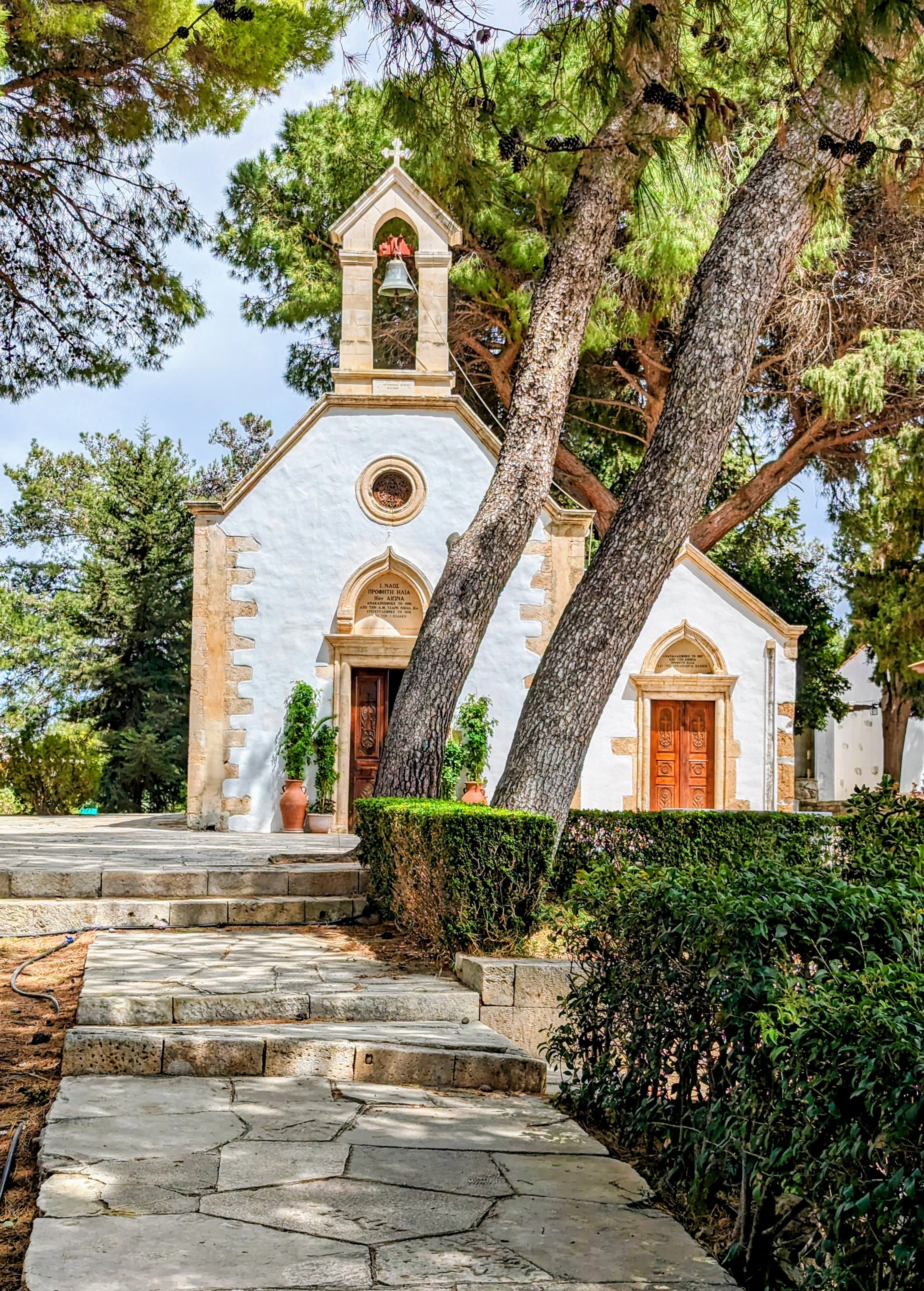 View of a stone path leading to a pretty small white and yellow church surrounded by trees