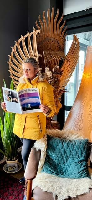 Advisor in a yellow jacket holding a book in front of a wooden structure