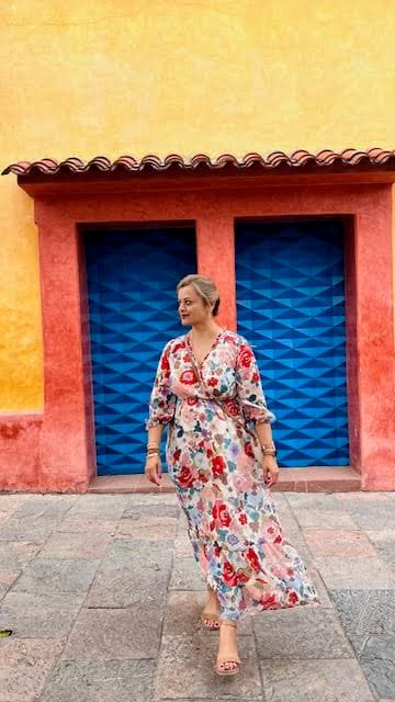 Advisor in a long floral print dress posing on the street in front of blue doors during the day